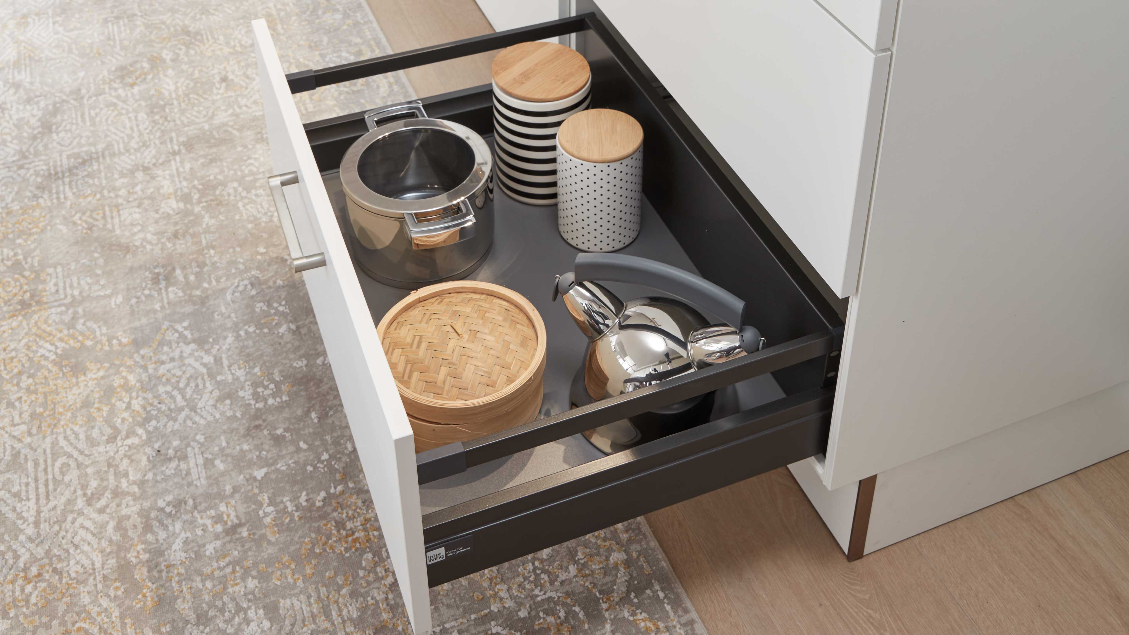 Offener weißer Schubkasten mit dunklem Innenrahmen, darin Edelstahlkanne und -topf, zwei Keramikdosen mit Holzdeckeln und ein Bambusdämpfer.