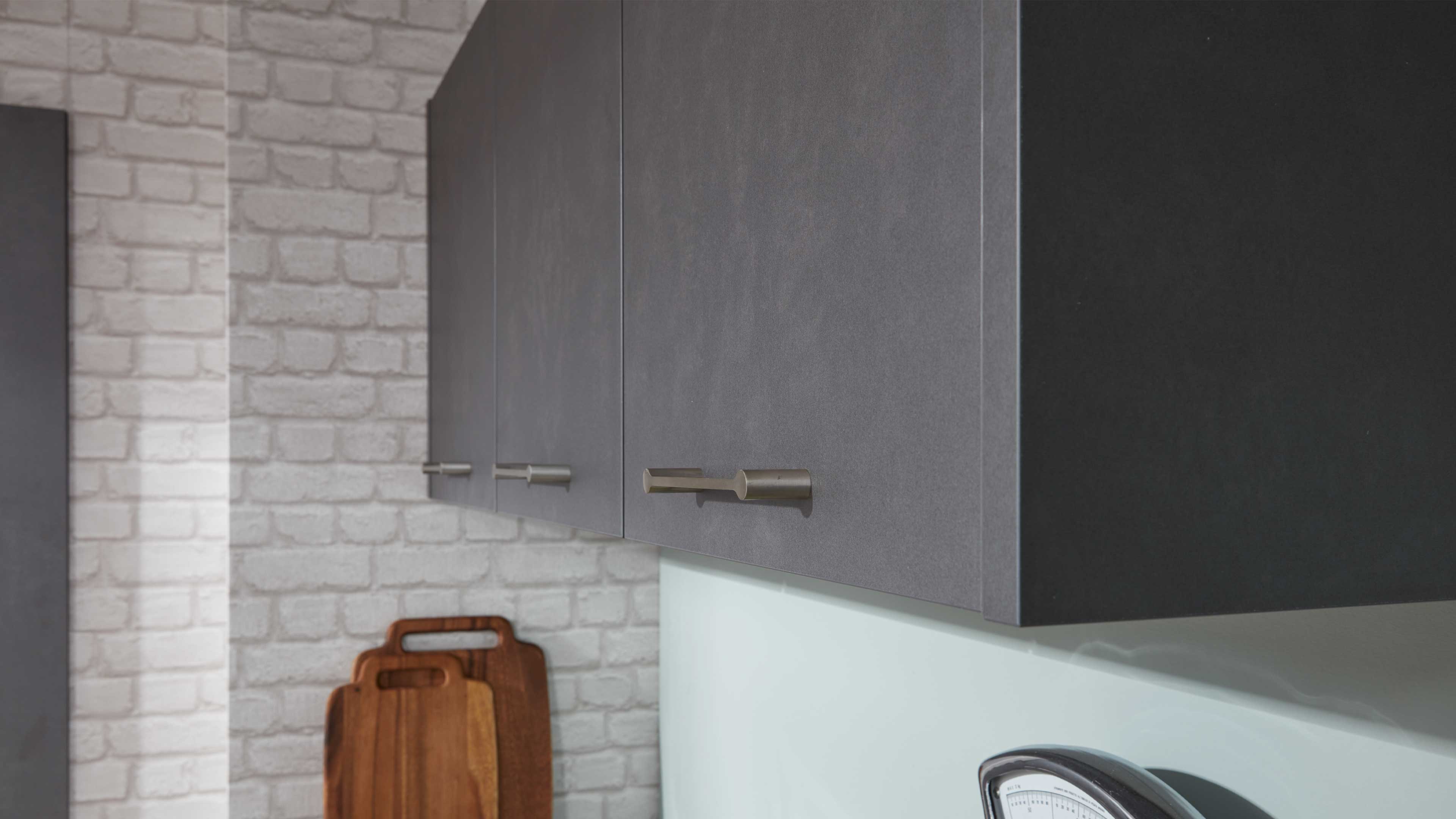 Graue matte Hängeschränke mit flachen Türen und langen, zylindrischen Metallgriffen, rechts Korpus in dunkelgrau.