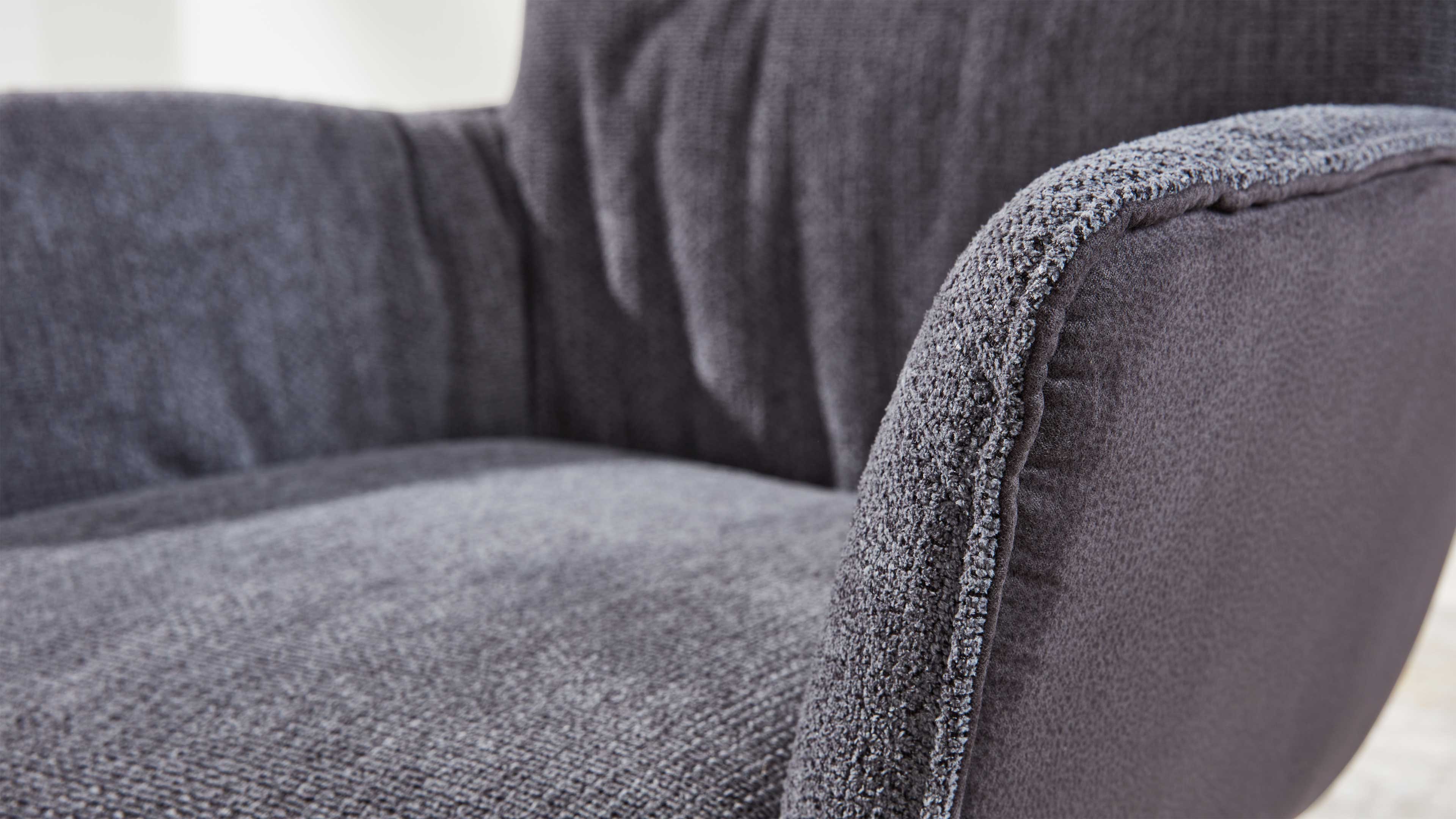 Nahaufnahme eines grauen Polstersessels, zeigt rechte Armlehne und Sitzfläche mit grob strukturierter, gewebter Oberfläche.