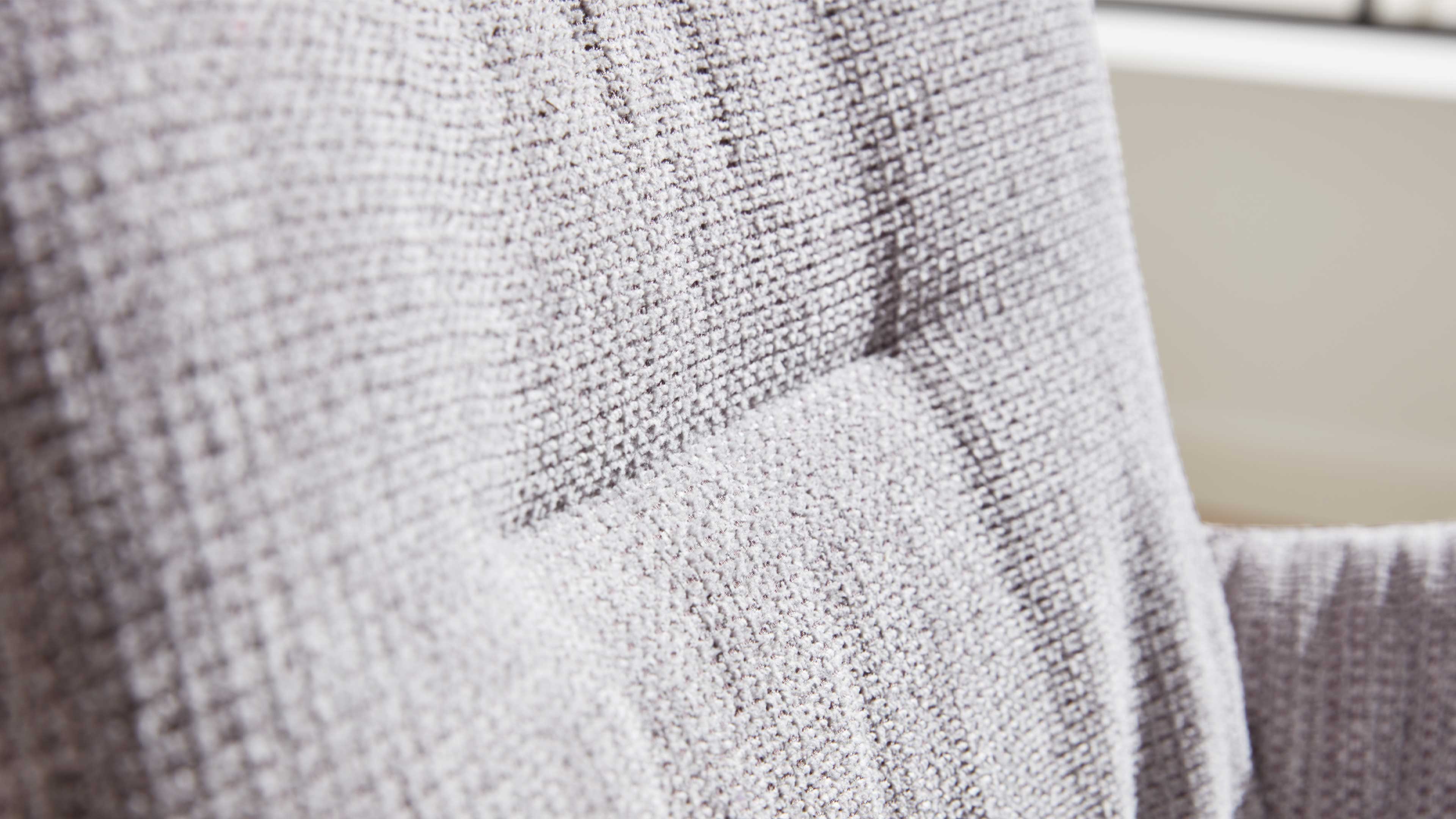 Rückenlehne eines hellgrauen Polstersessels mit grober gewebter Struktur, sichtbaren Nähten und leicht ausgeprägten Abnähern.