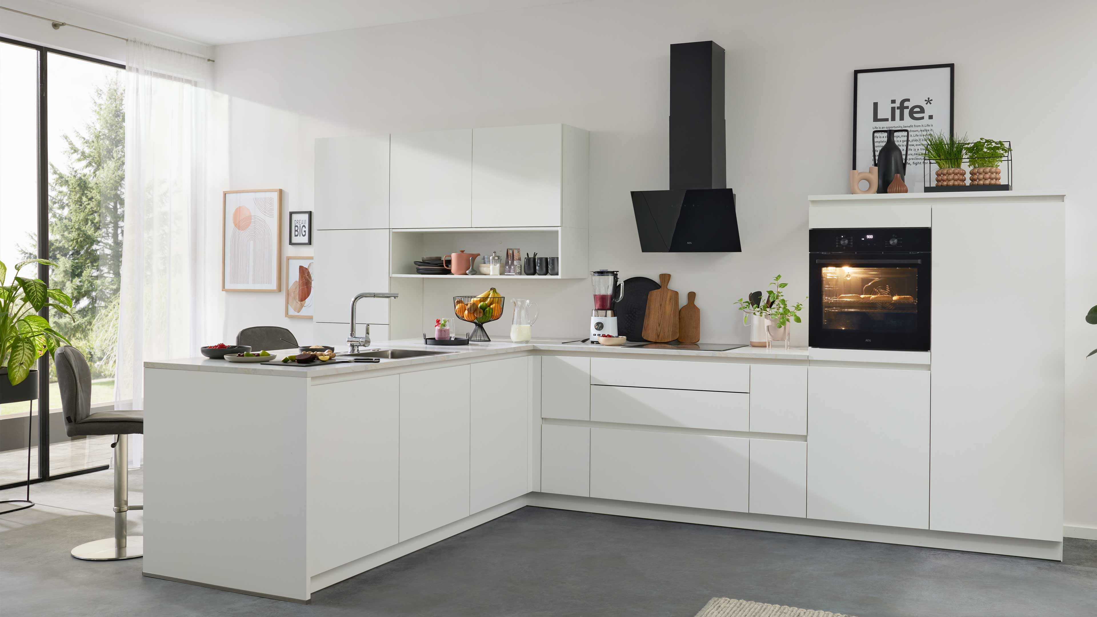 Weiße L-förmige Einbauküche mit Insel, schwarzer Wandhaube, eingebautem Ofen, Spüle, Obstschale und Küchenutensilien.
