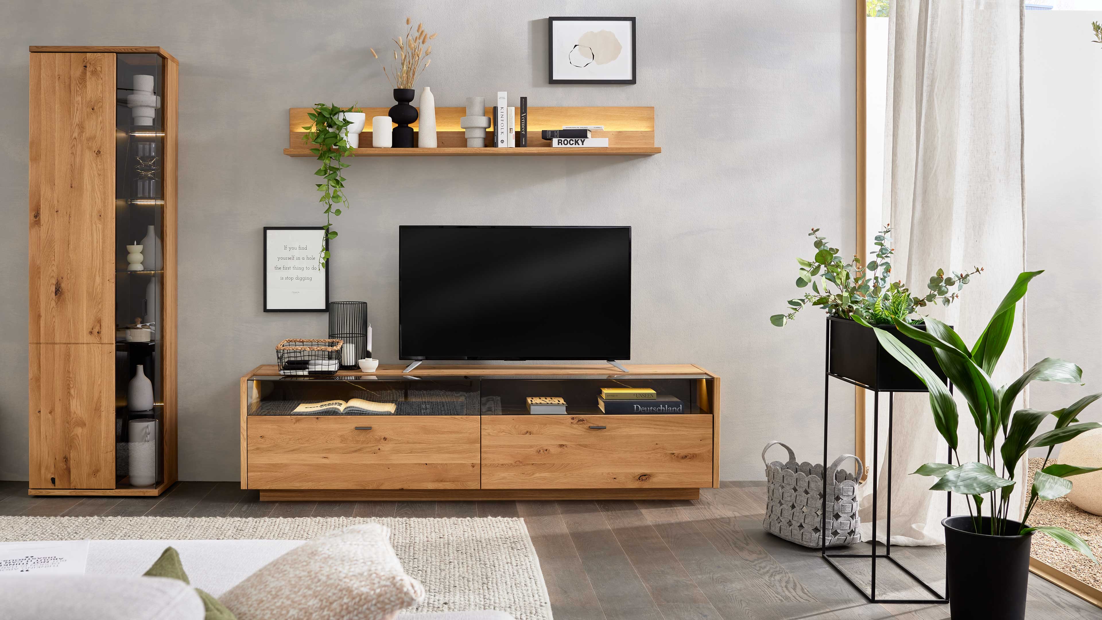 Wohnlösung mit TV-Board, hoher Vitrine und Wandregal mit grauen Glaselementen und Asteiche