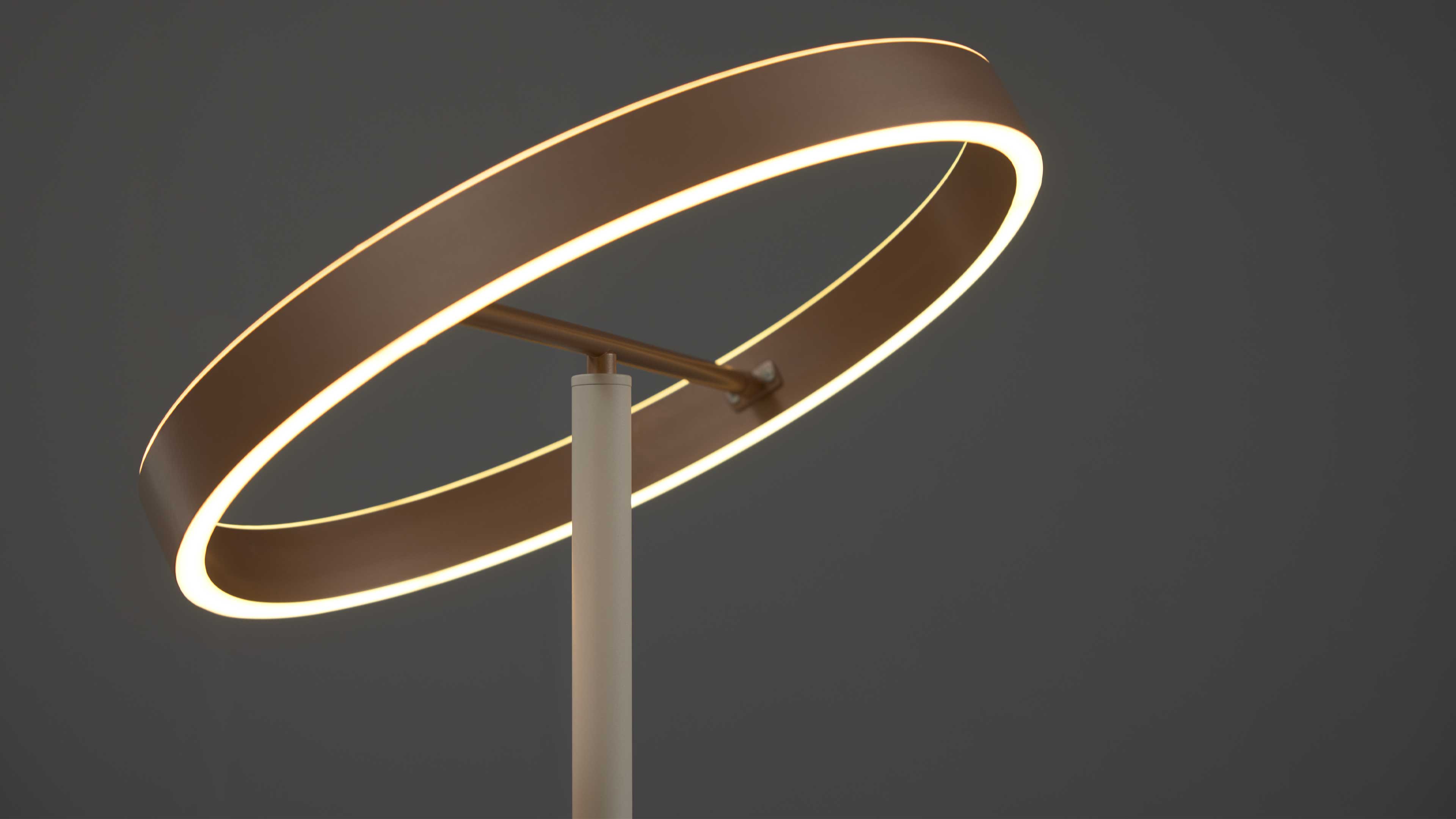 Ringförmige Leuchte mit durchgehendem warmweißem Leuchtrand, befestigt an schlanker Standstange mit Querarm vor dunkelgrauem Hintergrund.