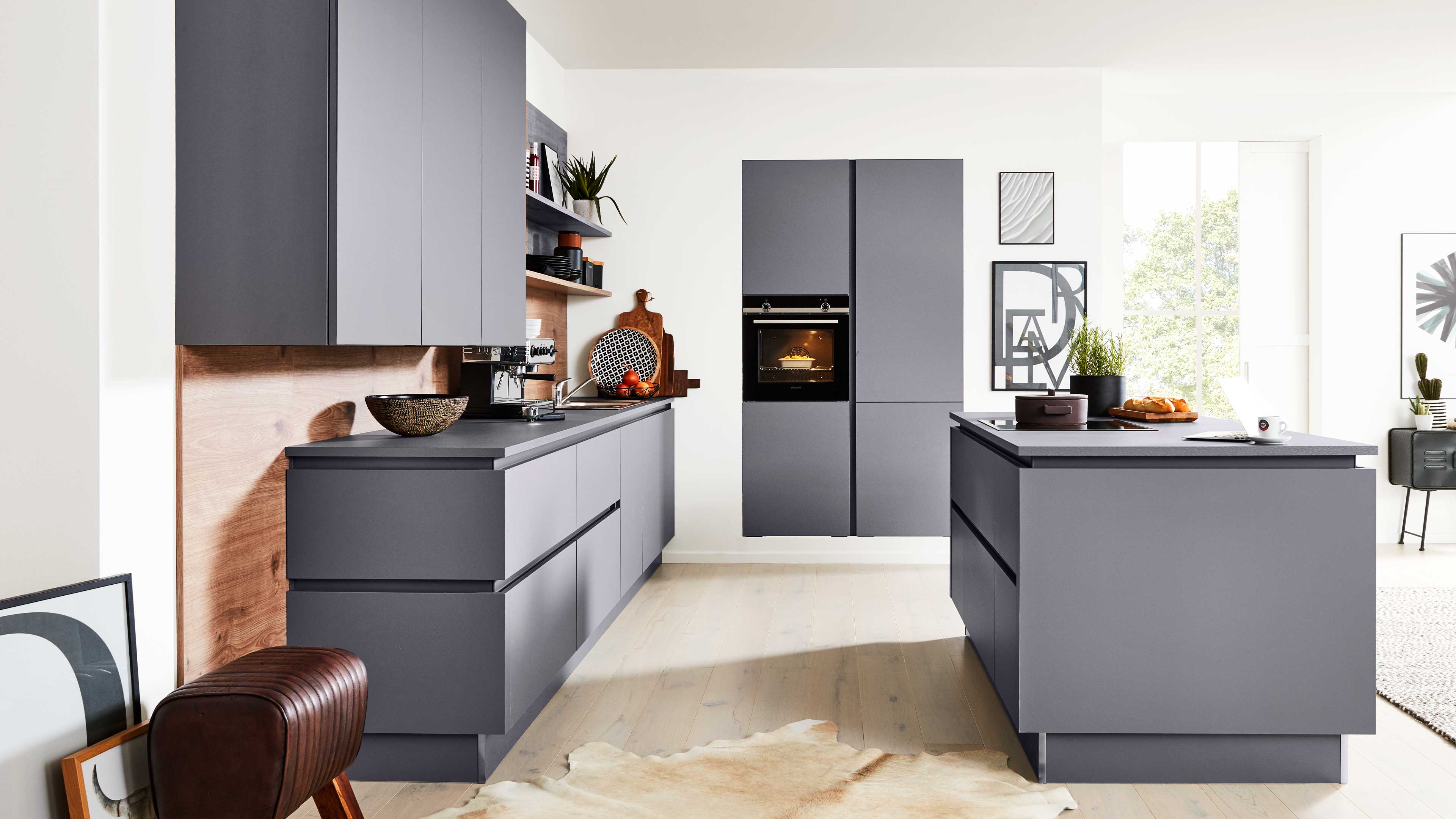 Graue matte Küchenzeile mit Insel, hängenden Oberschränken, eingebautem Ofen, Holzrückwand, offenem Regal und Fenster.