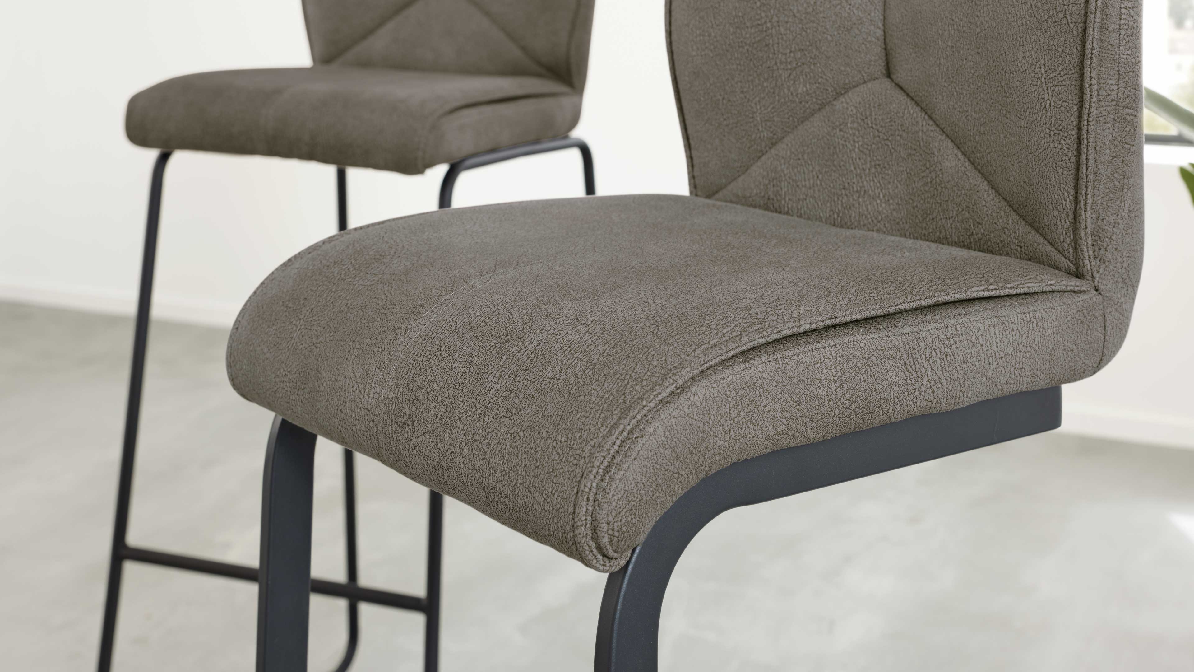 Gepolsterter Barhocker mit graubraunem, strukturiertem Stoffbezug, dekorativen Nähten und schwarzem Metallgestell.