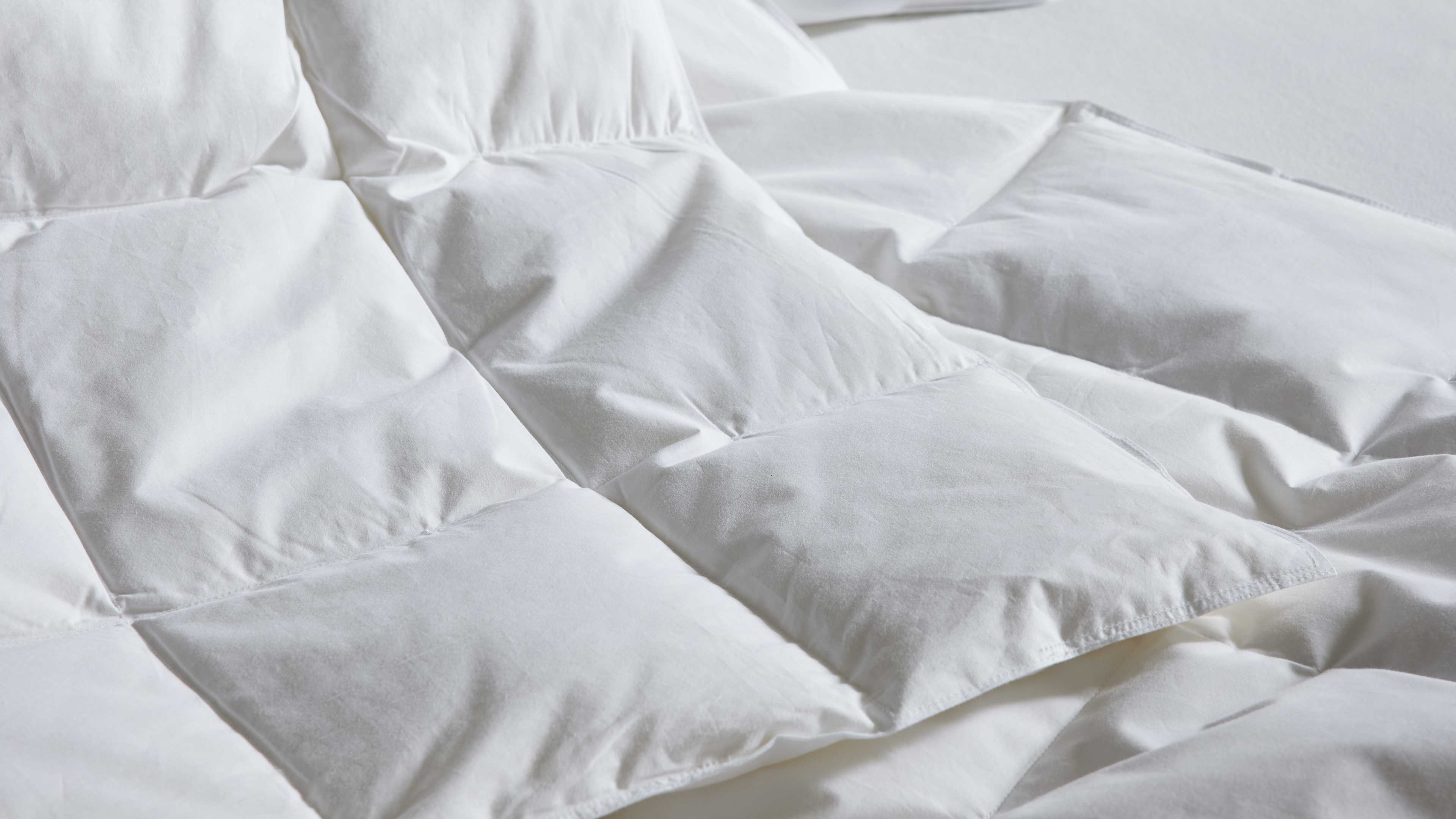 Weiß gesteppte Bettdecke mit großen quadratischen Kammern, leicht aufgebauscht, sichtbare Nähte und glatte Stoffoberfläche.