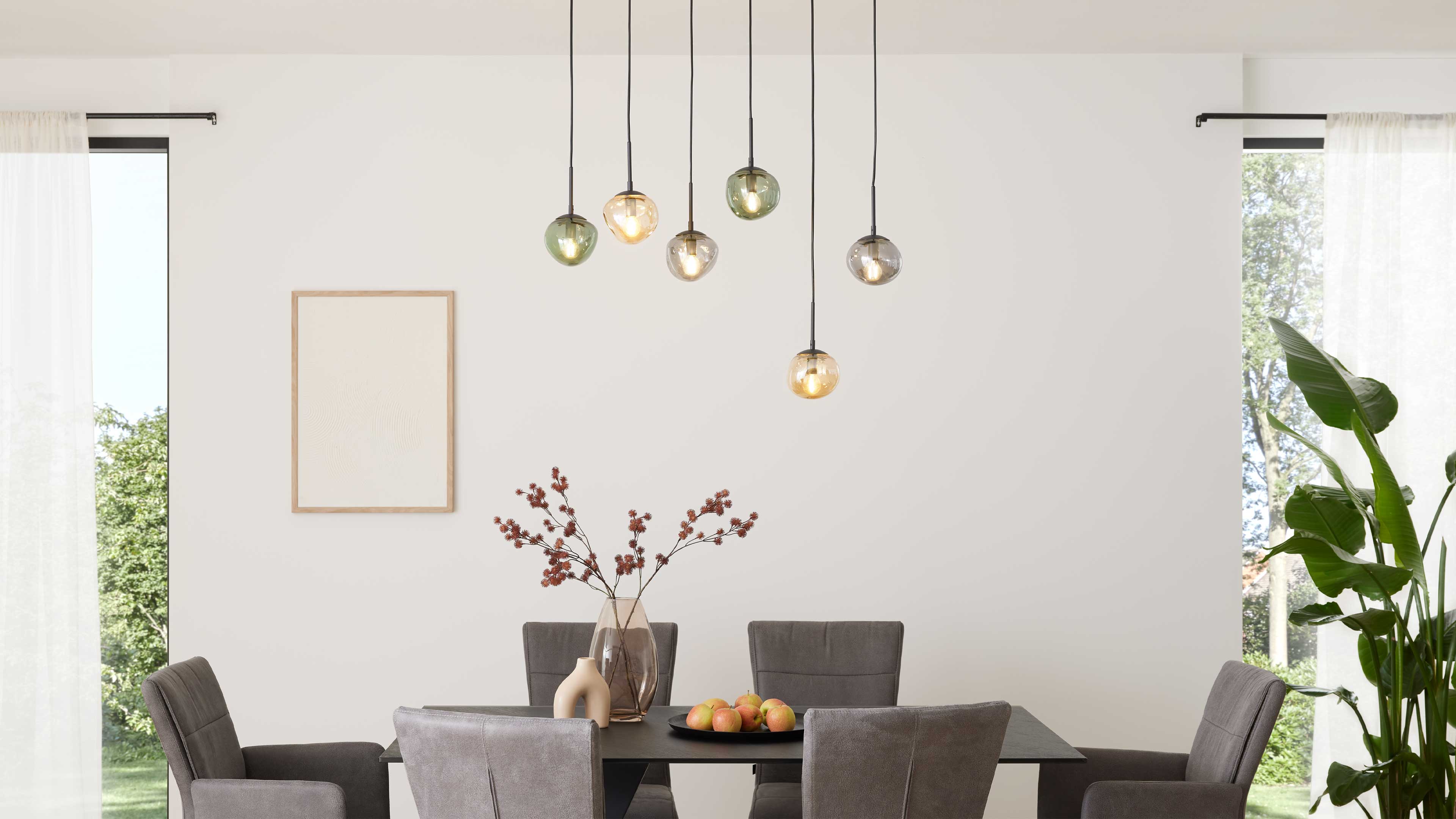 Esszimmertisch mit mehreren grauen Stühlen, schwarzer Tischplatte, Vase mit Zweigen, Obstschale und hängenden Glas-Pendelleuchten.