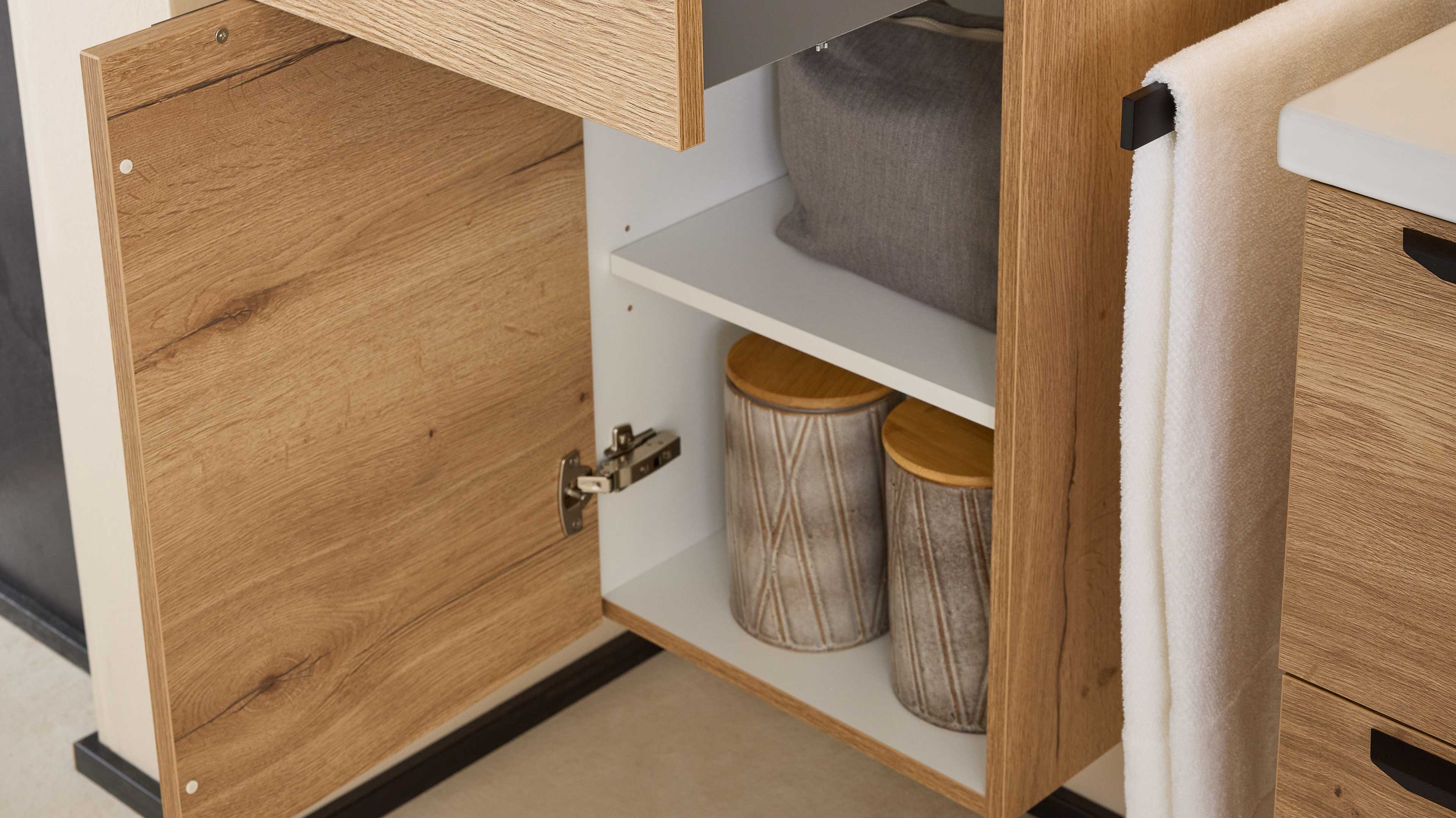 Geöffneter Eichen-Nachbildungsschrank mit weißer Innenablage, zwei keramischen Vorratsdosen und hängendem weißen Handtuch.