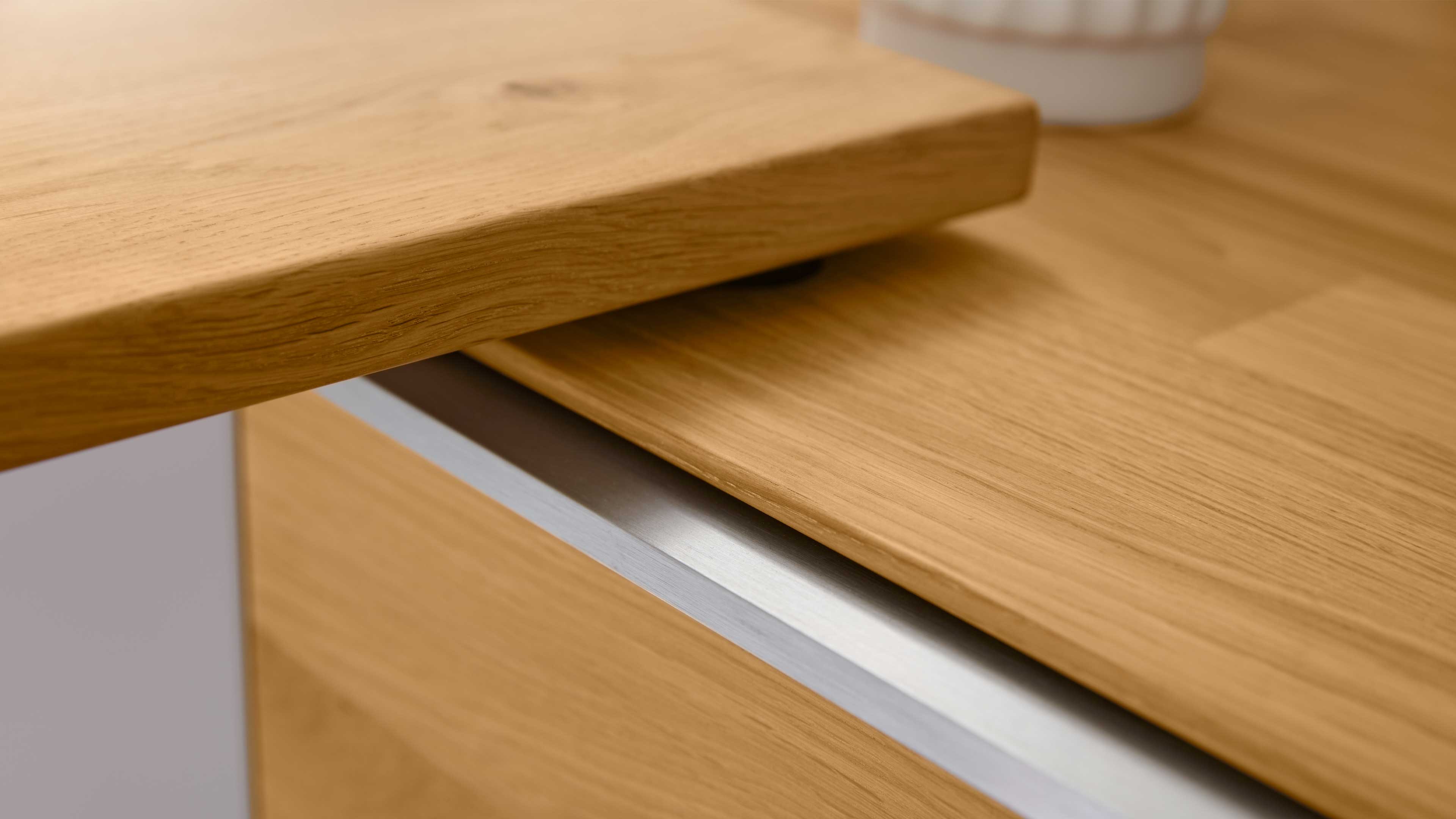 Holzplatte mit sichtbarer Maserung, über einer Frontplatte mit schlanker Aluminium-Griffleiste überstehend.