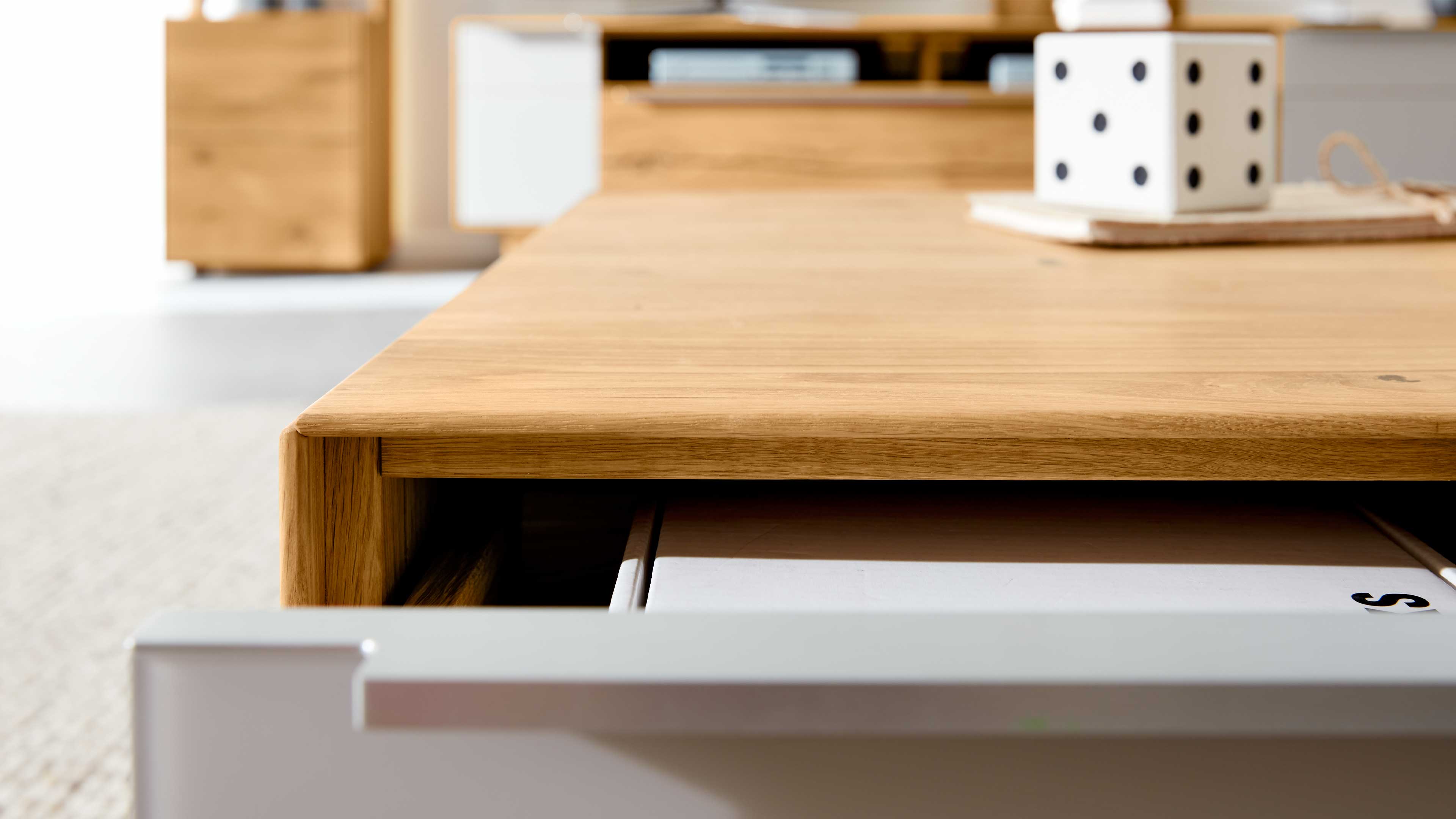 Niedrige Holz-Tischplatte mit offenem Schubfach, sichtbarer weißer Schubladenfront und einem Würfel mit schwarzen Punkten.