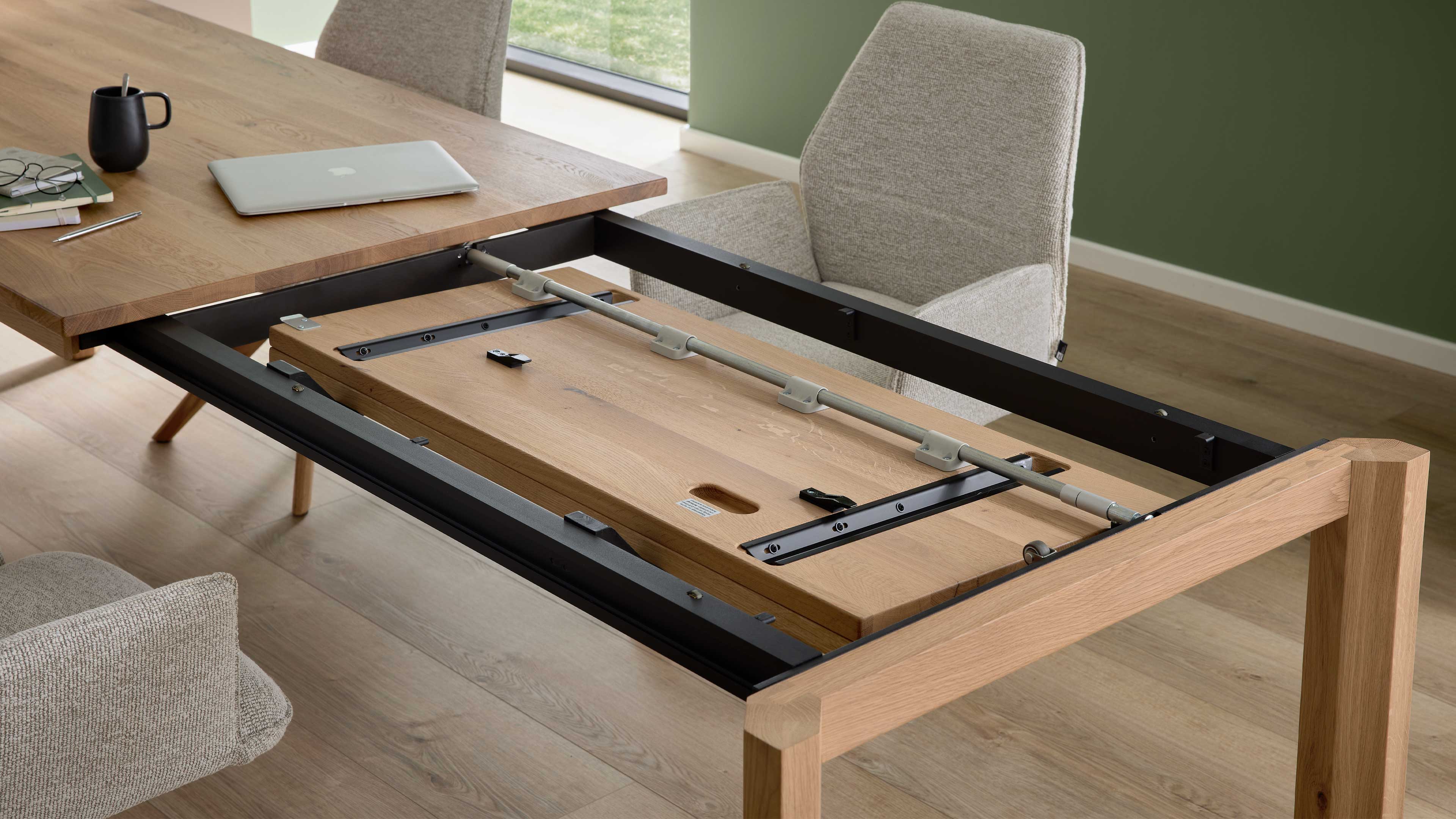 Ausgezogener Holztisch mit offenem Ausziehmechanismus und eingelegter Verlängerungsplatte, daneben zwei hell bezogene Stühle.