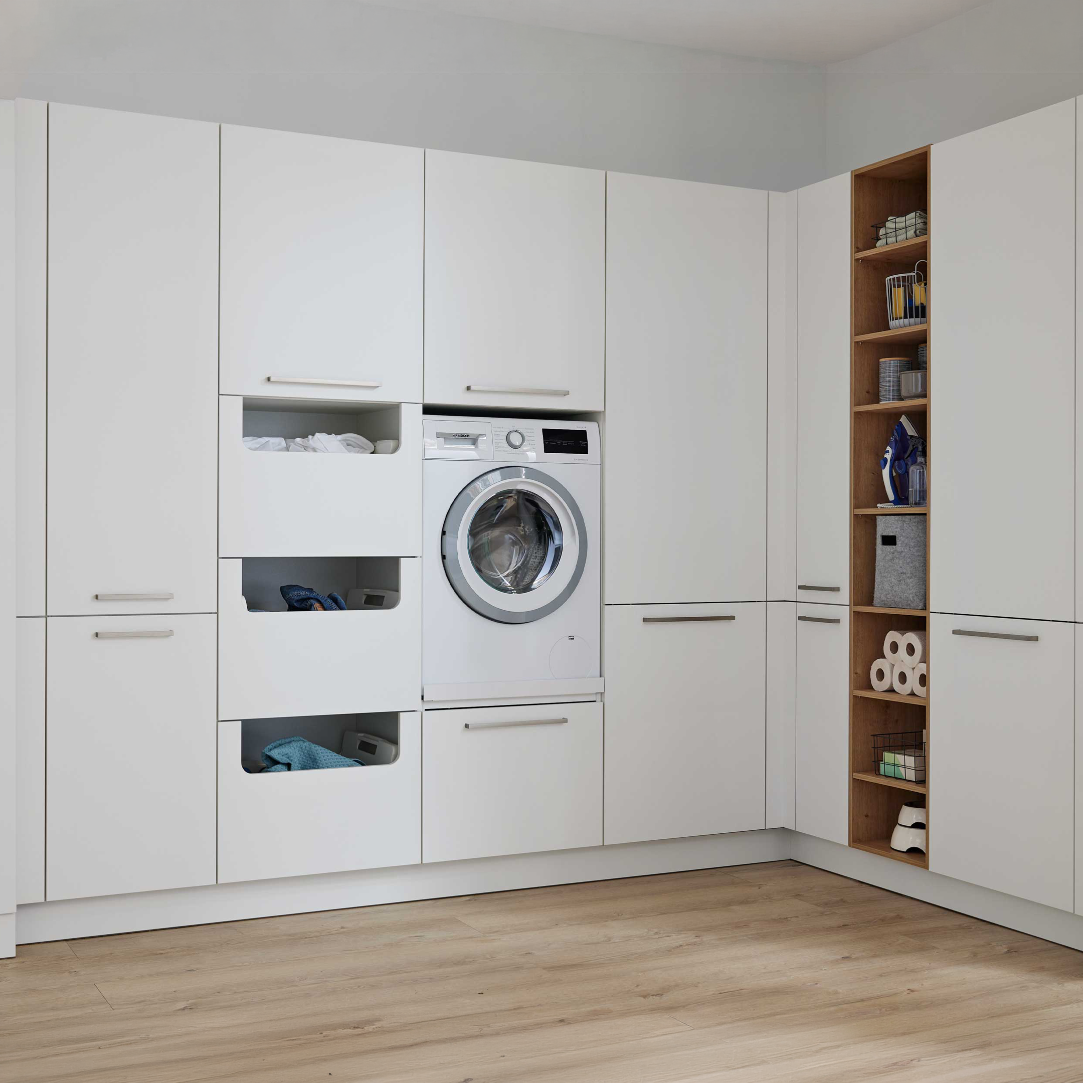 Weißer Einbauschrank mit Frontlader, offenen Wäscheschubladen und seitlichem Holzregal mit Bügeleisen, Toilettenpapierrollen und Boxen.