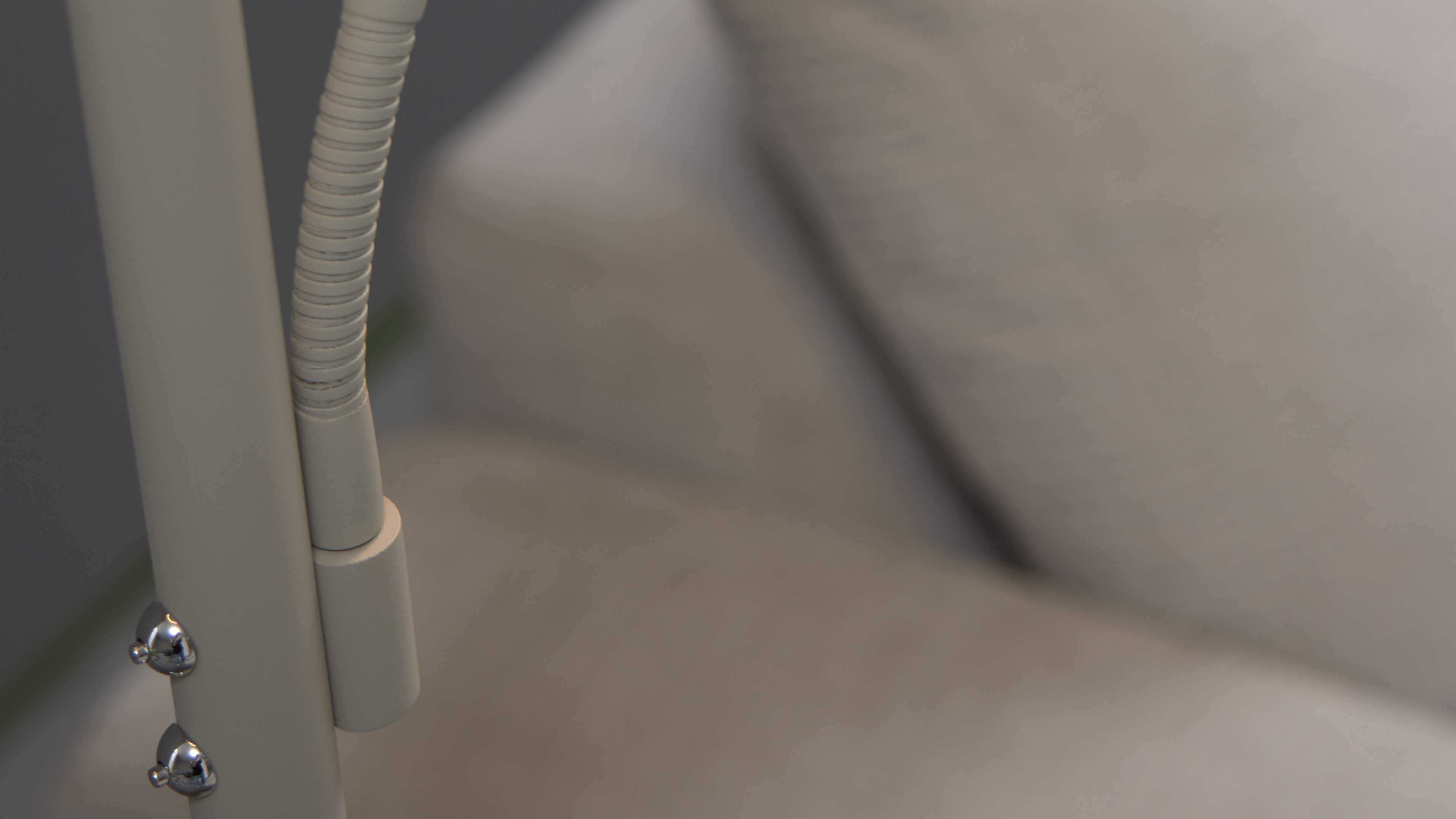 Detailaufnahme eines beigen Lampenstiels mit flexiblem Schwanenhals und zwei chromglänzenden Kugelgelenken vor unscharfem beigen Sofa.