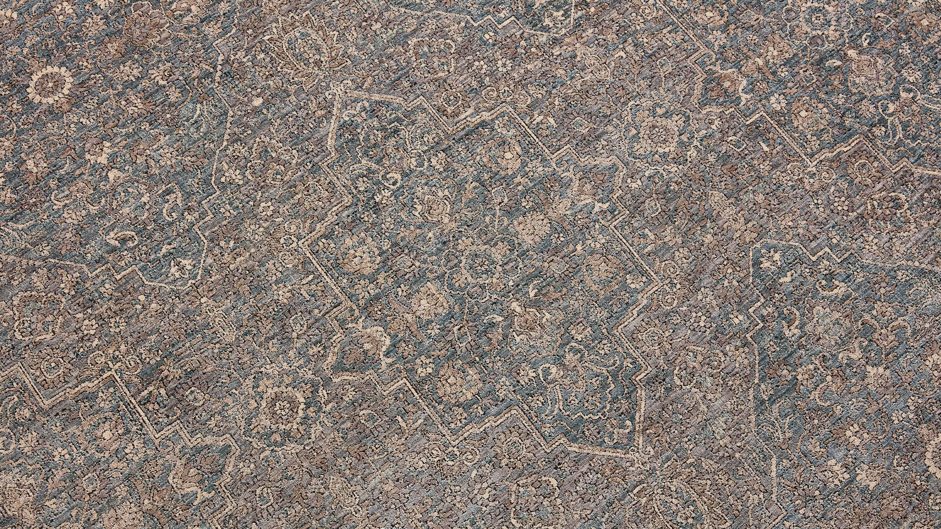 Teppich mit zentralem sternförmigem Medaillon und dichtem Blumen- und Rankenmuster in gedeckten Blau- und Beigetönen.