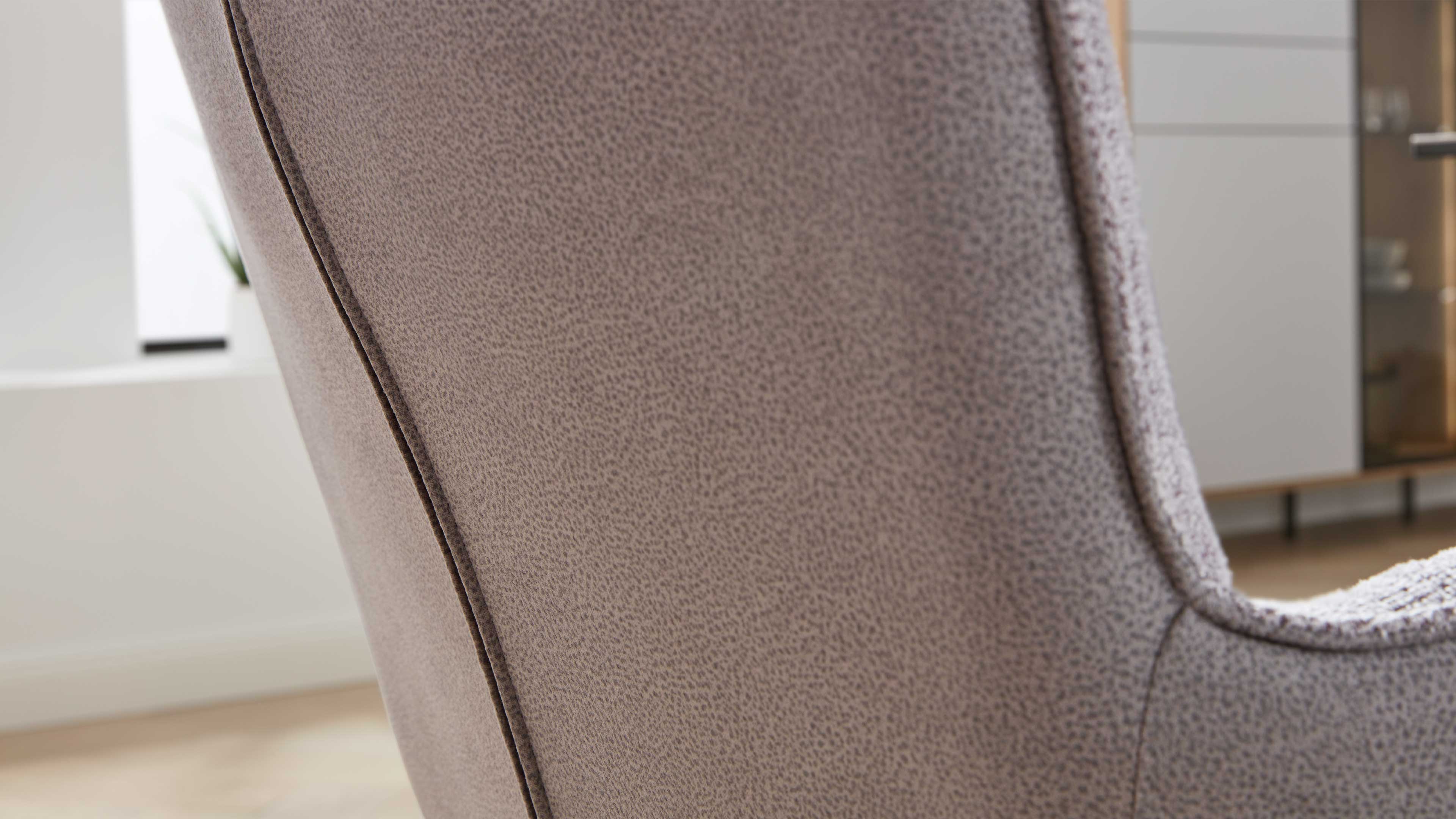 Nahaufnahme der Rückenlehne eines gepolsterten Sessels aus beige-grauem, strukturiertem Stoff mit sichtbarer Ziernaht.