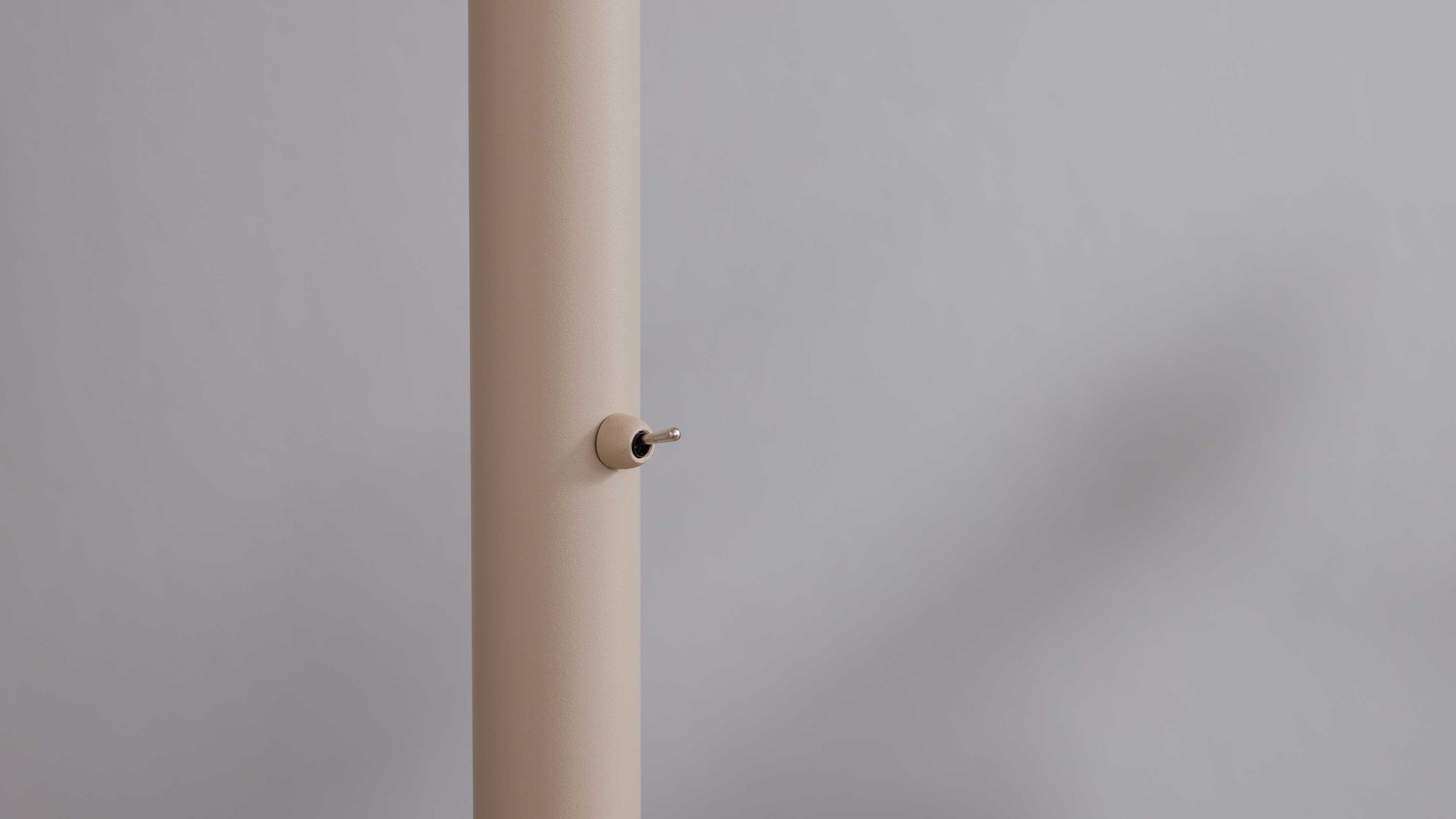 Beige zylindrische Stange mit kleinem silberfarbenem Kippschalter an der Seite, vor einer hellgrauen Wand.