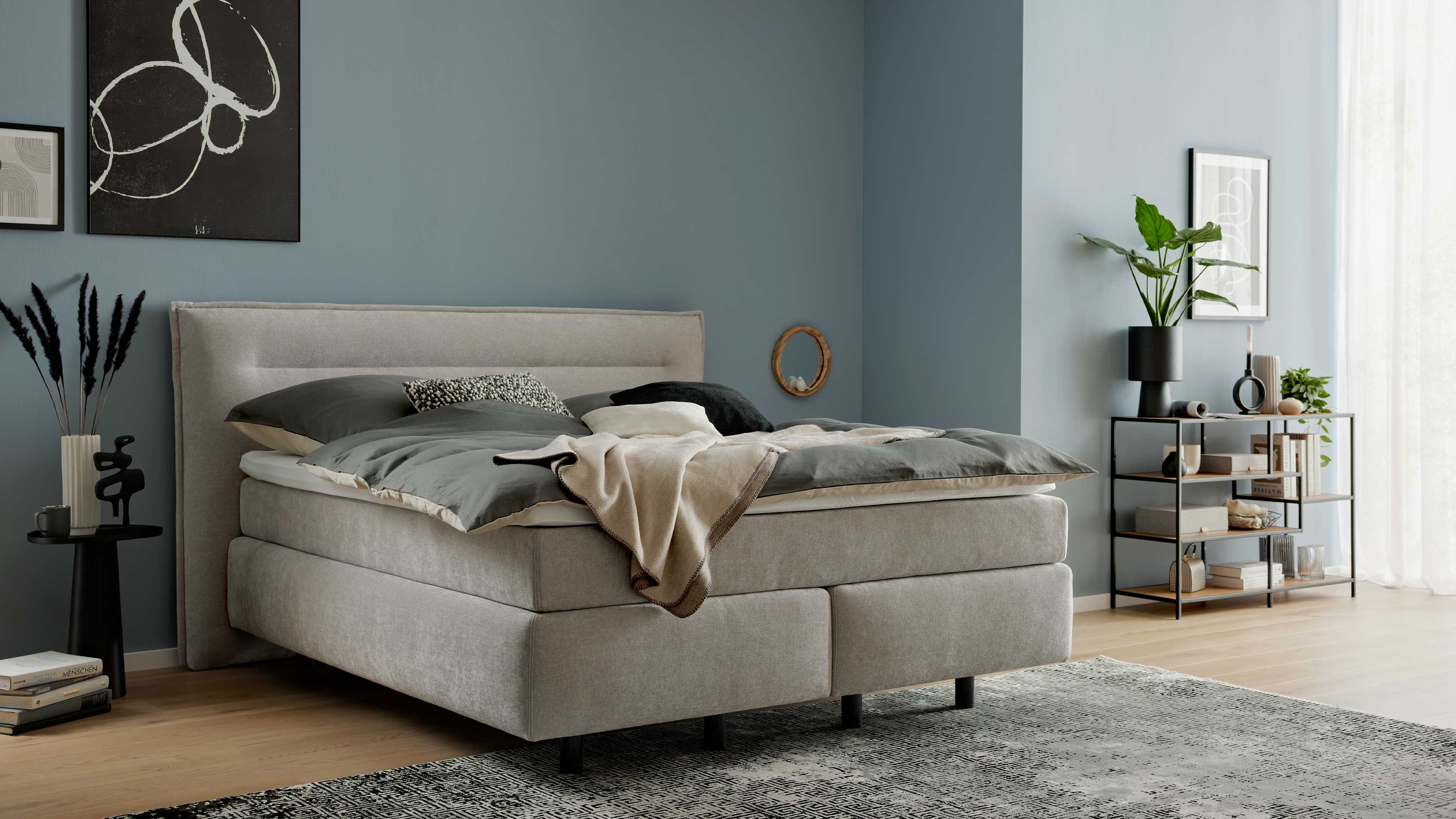 Boxspringbett mit gepolstertem Kopfteil, grauem Stoffbezug und durchgehender Liegefläche für stabilen Schlafkomfort