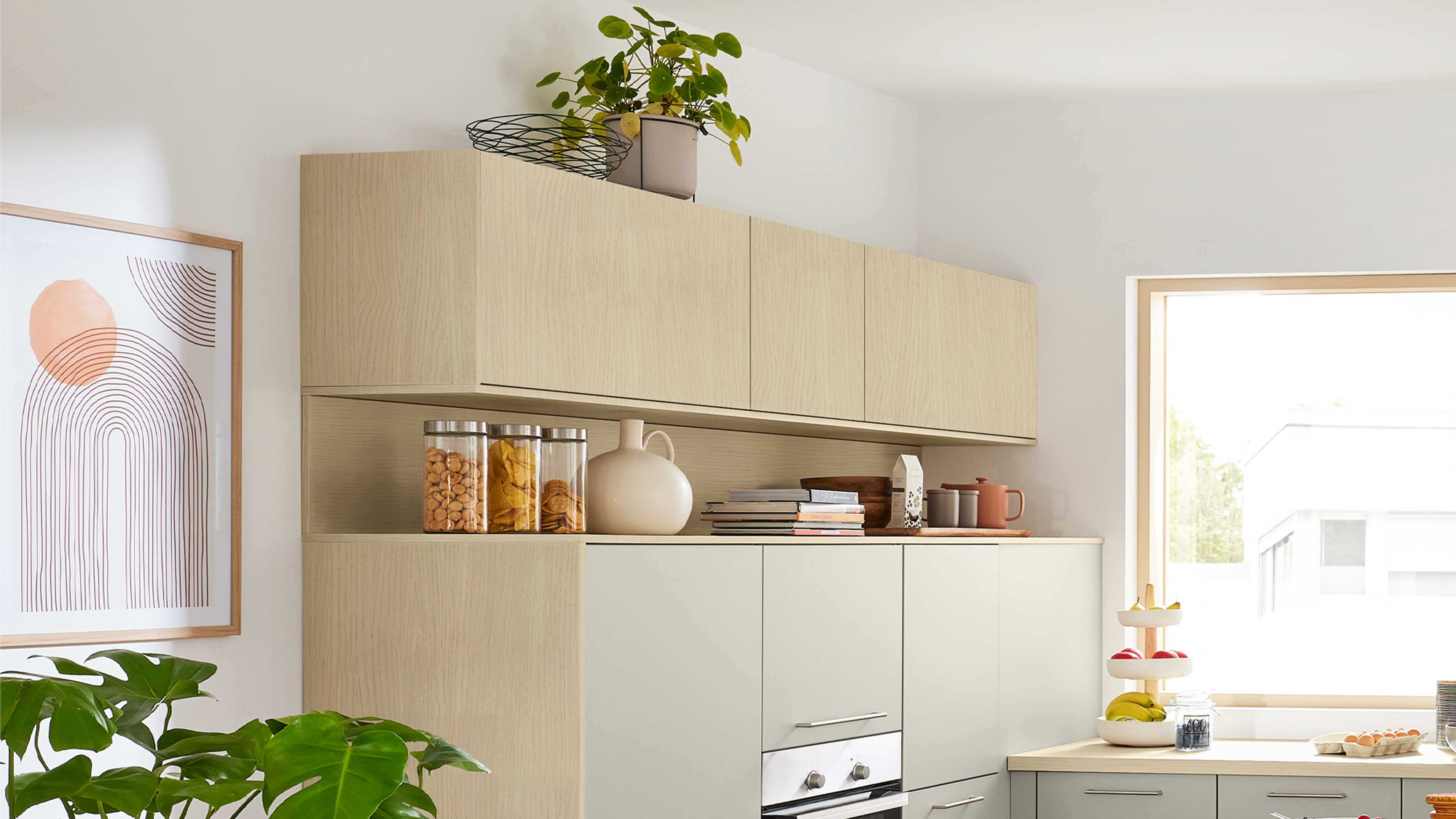 Helle Holz-Hängeschränke mit offener Ablage, darunter matte graue Unterschränke mit Einbaubackofen und Arbeitsfläche.