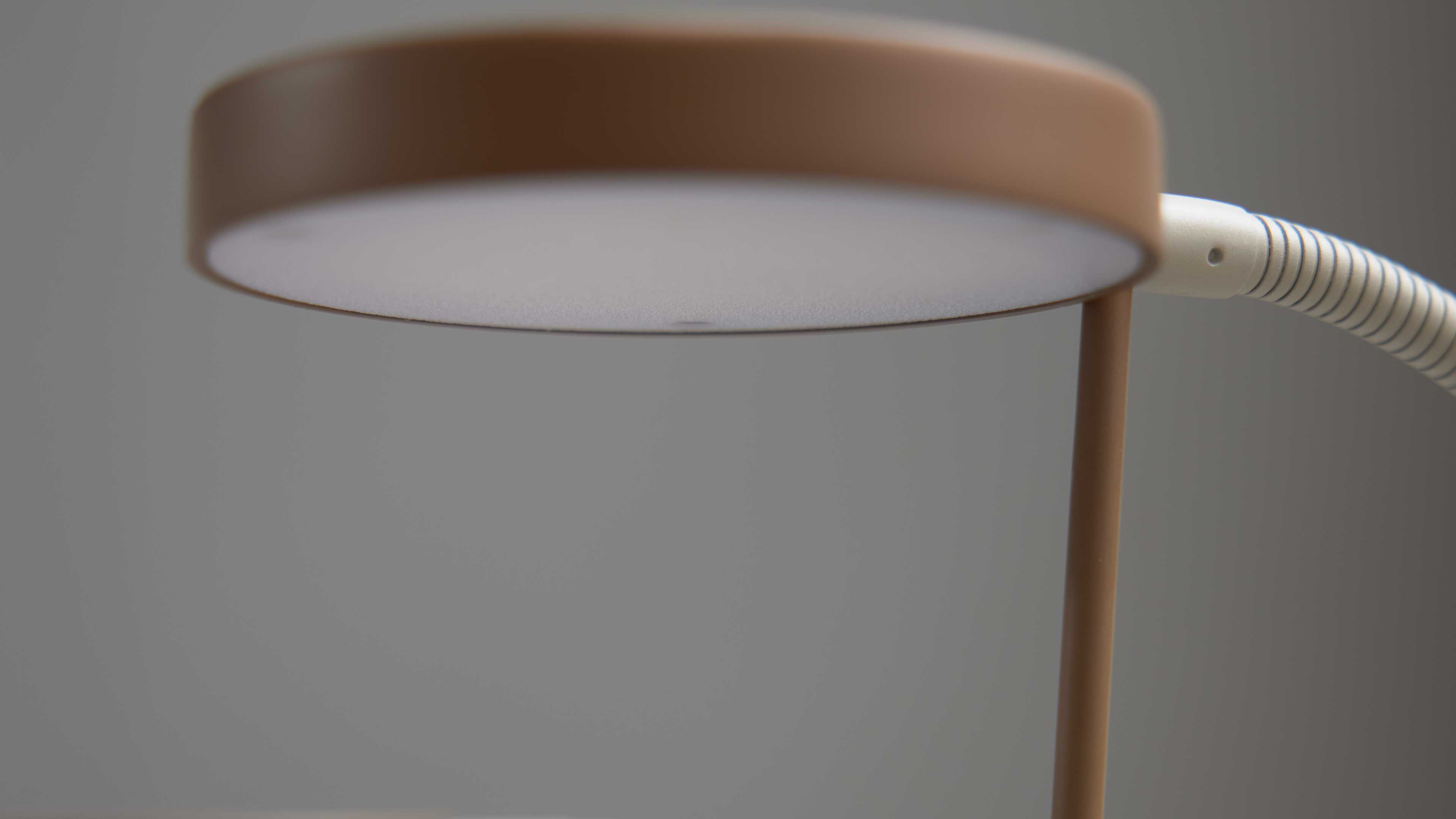 Tischlampe mit flachem, rundem, beigefarbenem Lampenschirm und weißer Diffusor, schlanker Stab und gestreifter flexibler Arm.