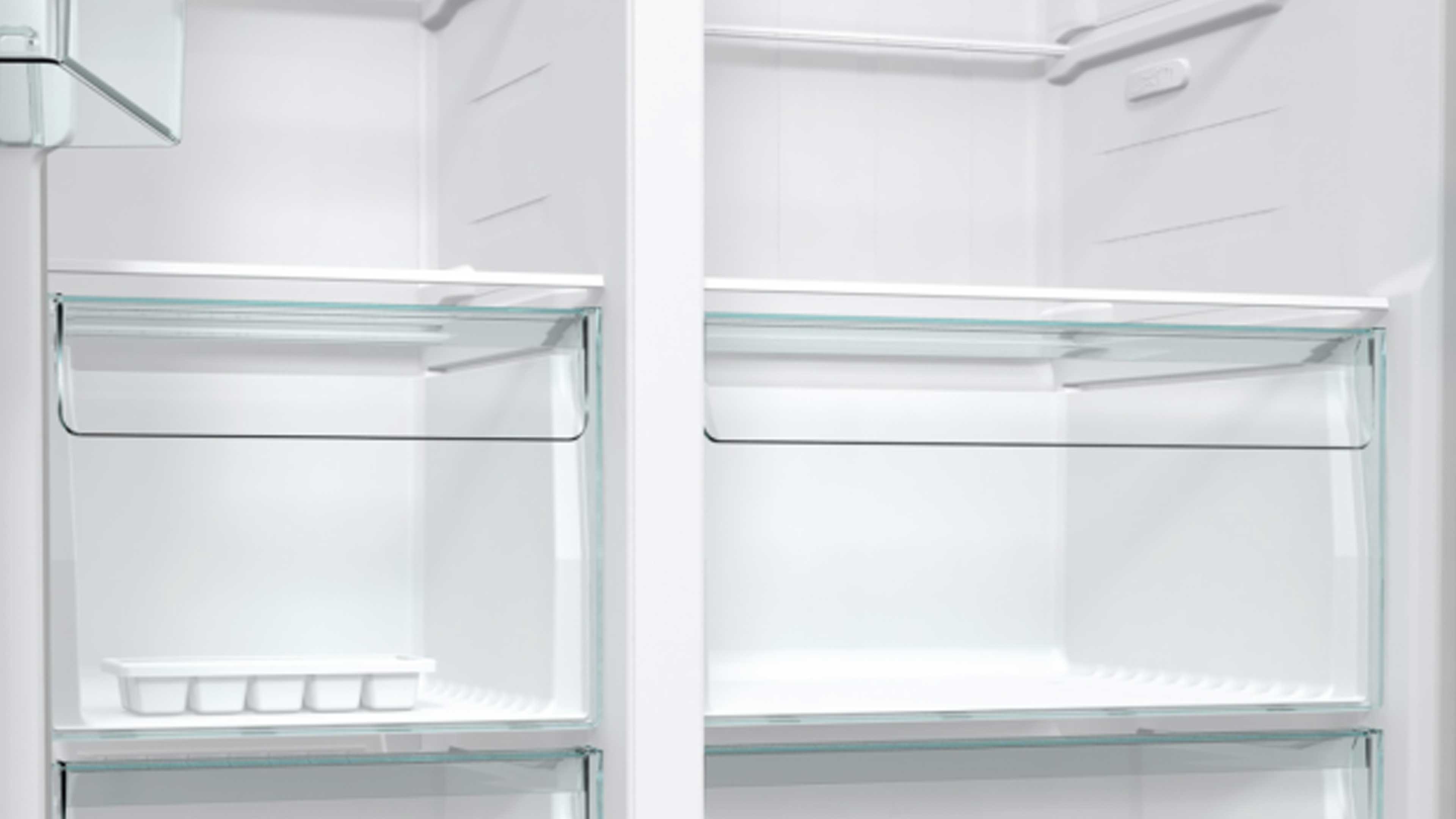 Innenraum eines weißen Kühlschranks mit mittiger Trennwand, zwei transparenten Schubladen aus Glas und einem weißen Eiswürfelfach links.