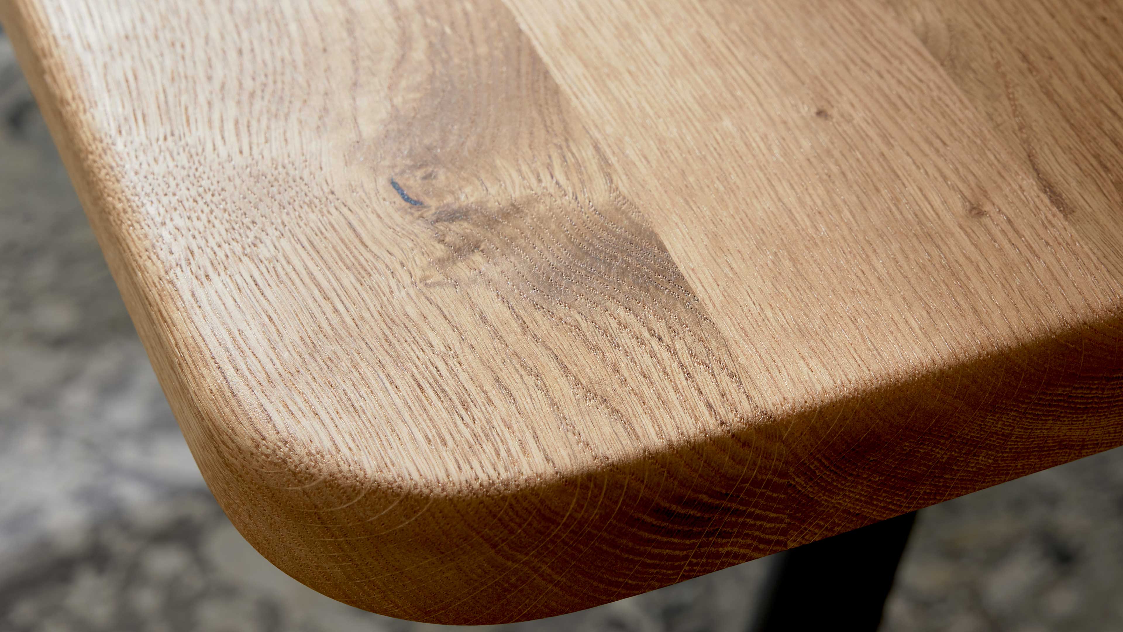 Abgerundete Tischplatte aus hellbraunem Holz mit sichtbarer Jahresringstruktur, Maserung und kleinem Knoten.