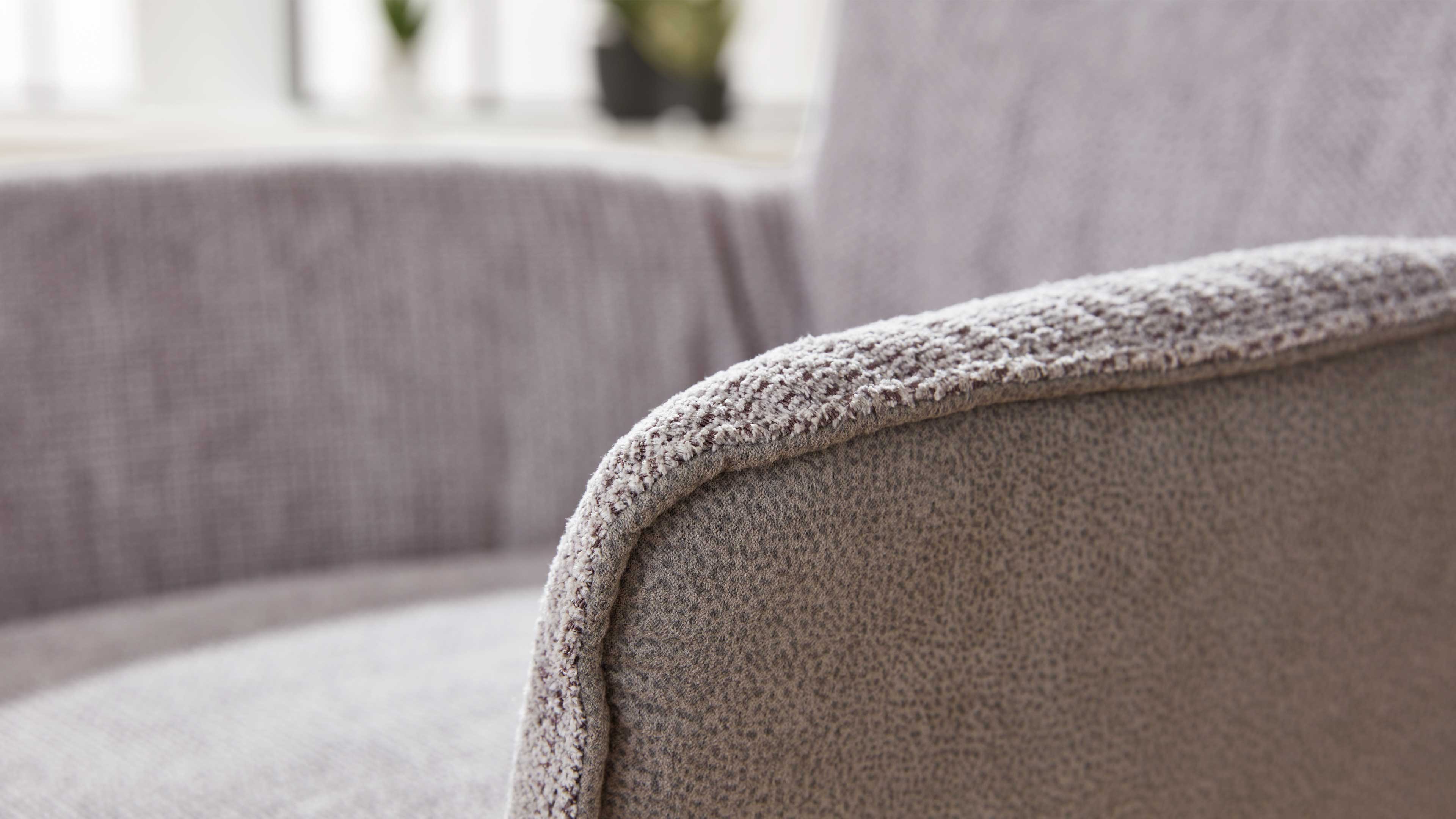 Nahaufnahme einer gepolsterten Armlehne eines Sitzmöbels mit strukturierter beige-grauer Stoffoberfläche, im Hintergrund unscharfe Rückenlehne.