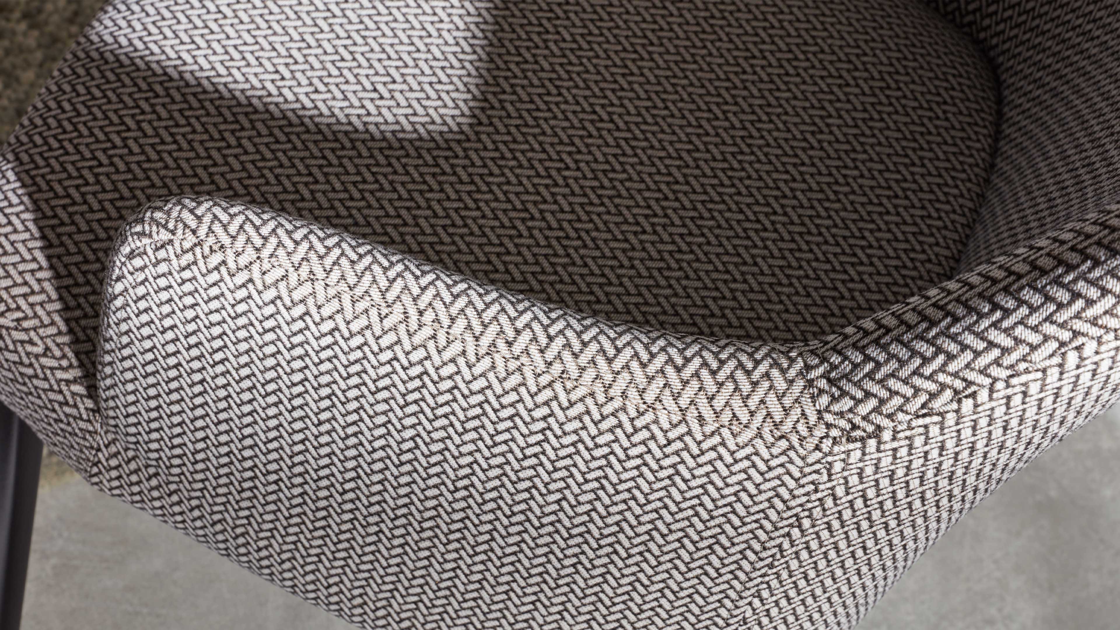 Gepolsterter Stuhl mit hellbeigem Stoff in fein zickzackigem Gewebemuster und sichtbarer Naht an der Kante.