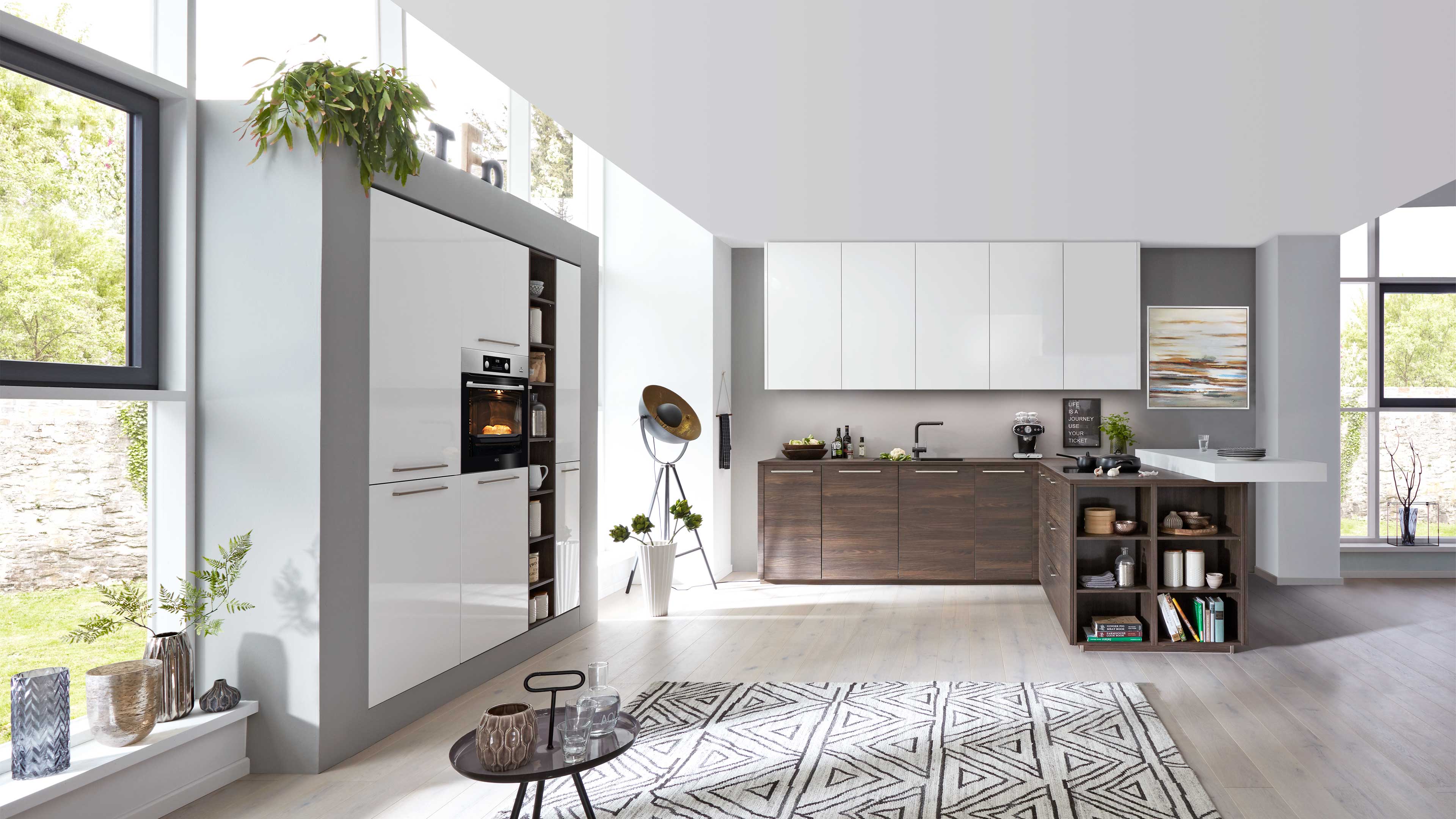 Offene Küche mit weiß glänzenden Oberschränken, dunklen Holzunterschränken, Insel mit offener Regalseite und eingebautem Backofen.