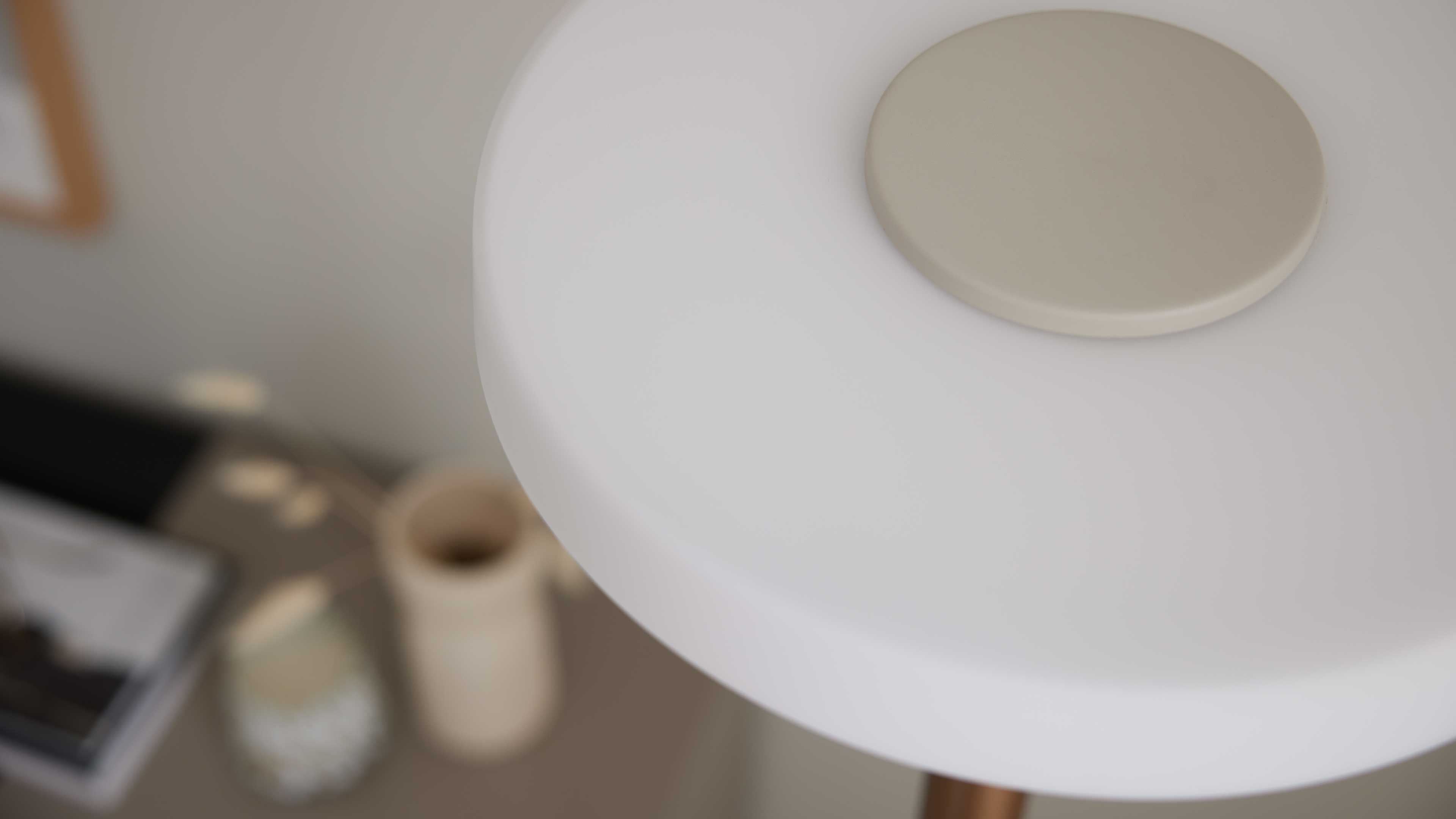 Weißes rundes Beistelltisch-Plateau mit beige rundem Aufsatz oben rechts, im Hintergrund unscharfe Vasen, Kerze und Buch.