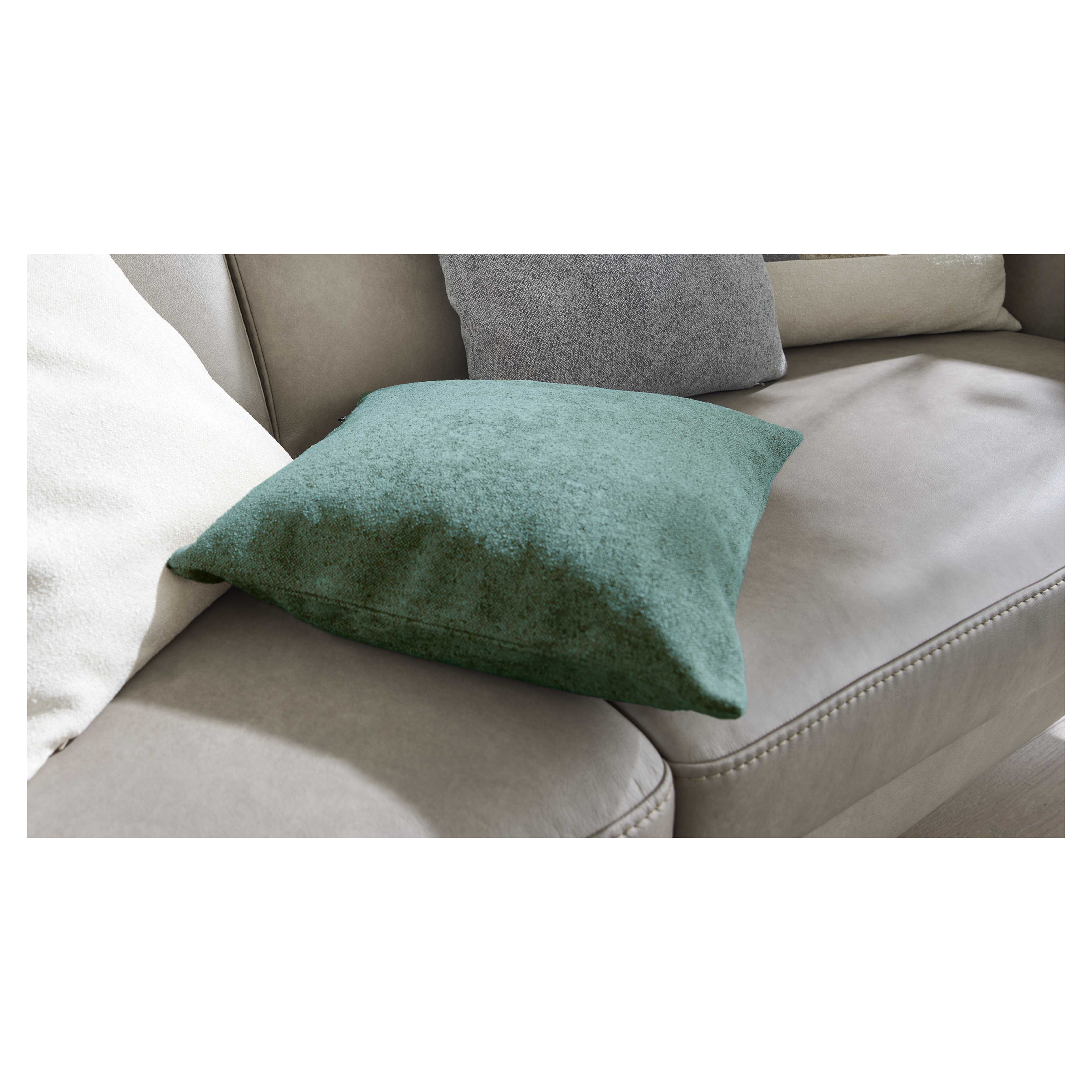 Grünes, quadratisches Kissen liegt auf einem hellbeigen Ledersofa, links ein weißes und hinten ein graues Kissen.