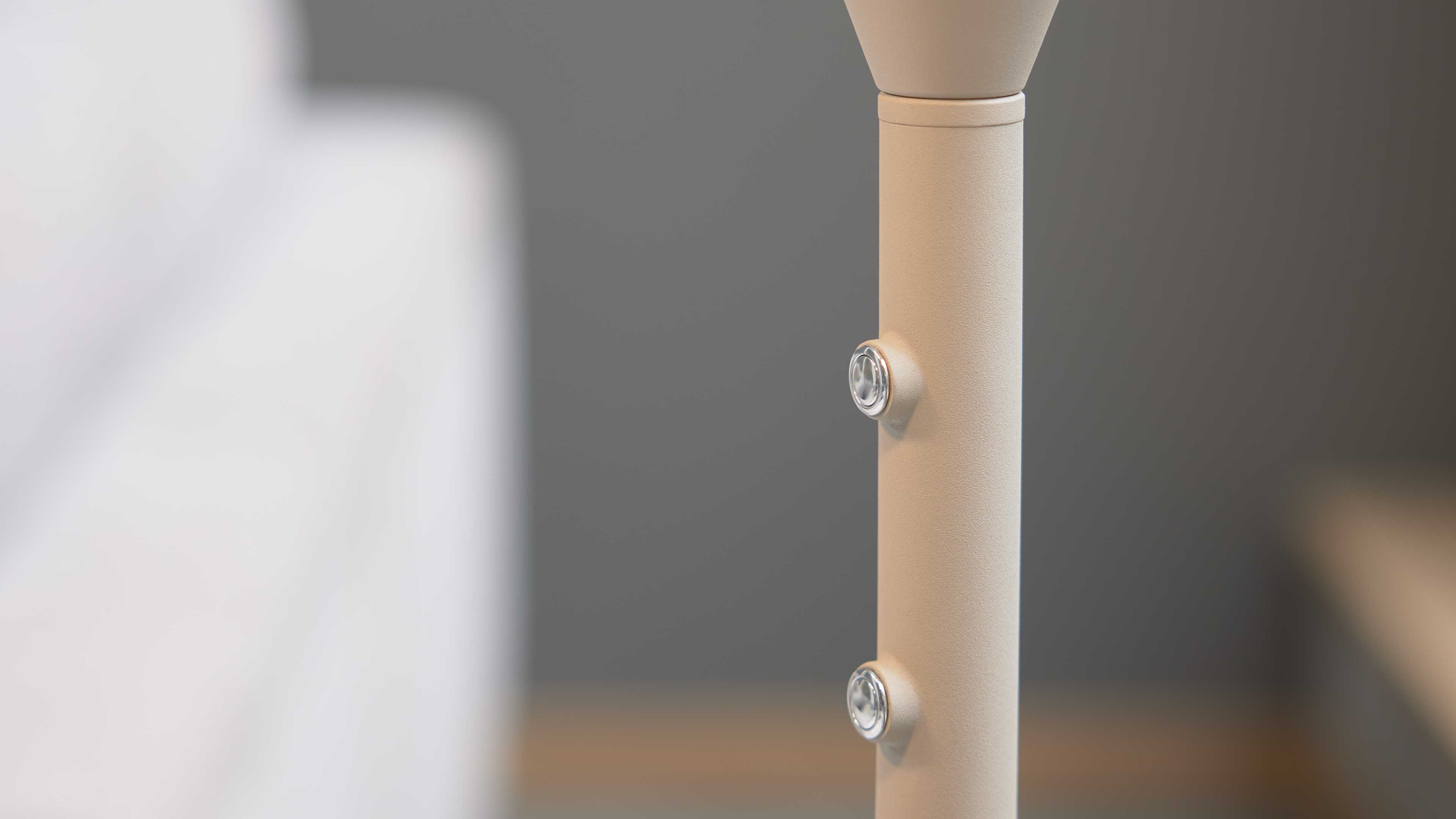 Beige senkrechte Stange mit zwei runden transparenten Druckknöpfen, unscharfer grauer Hintergrund.