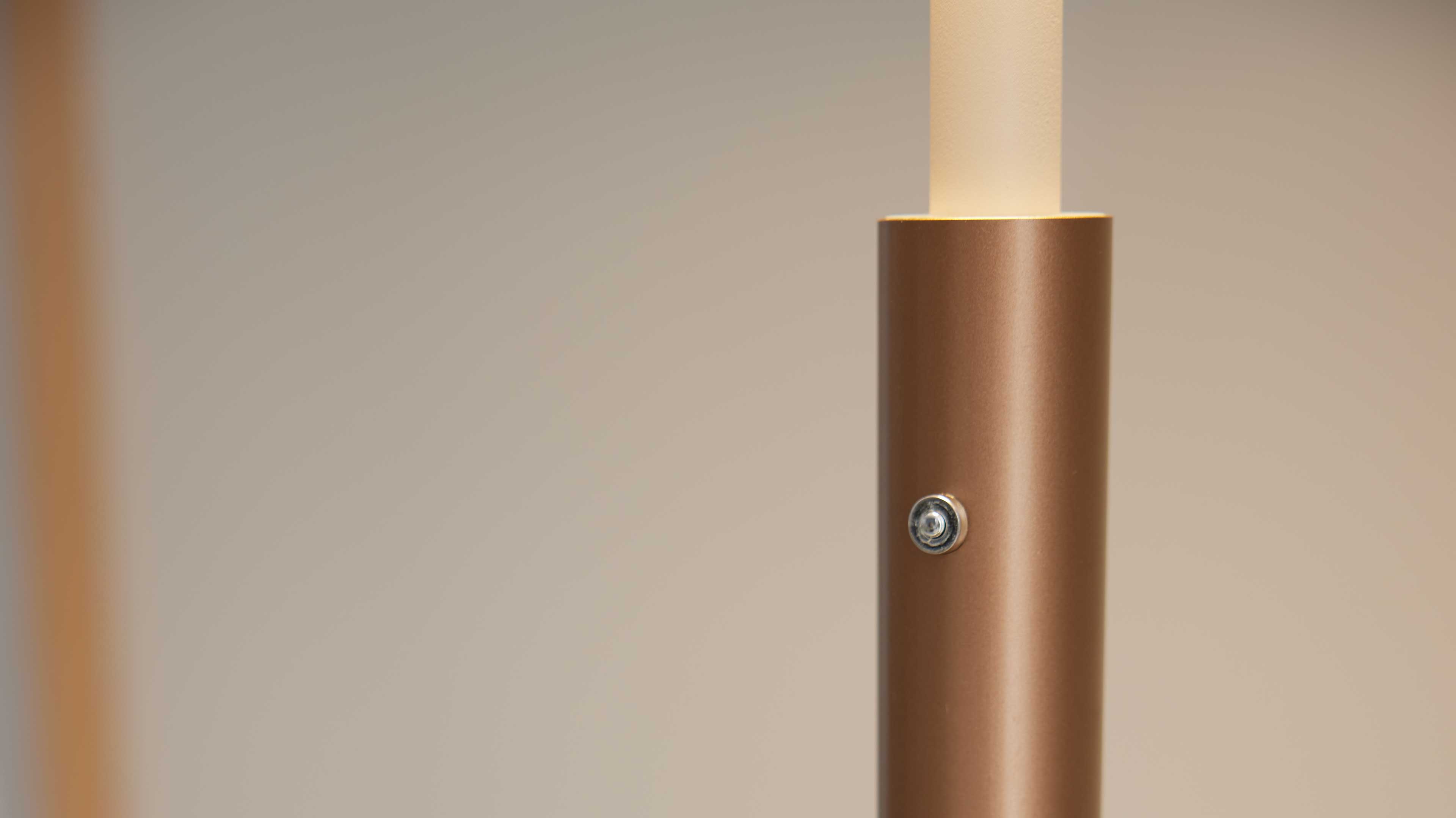 Zylindrischer, bronzefarbener Metallstab einer Lampe mit sichtbarer Schraube und oben angesetztem beigen Diffusor.