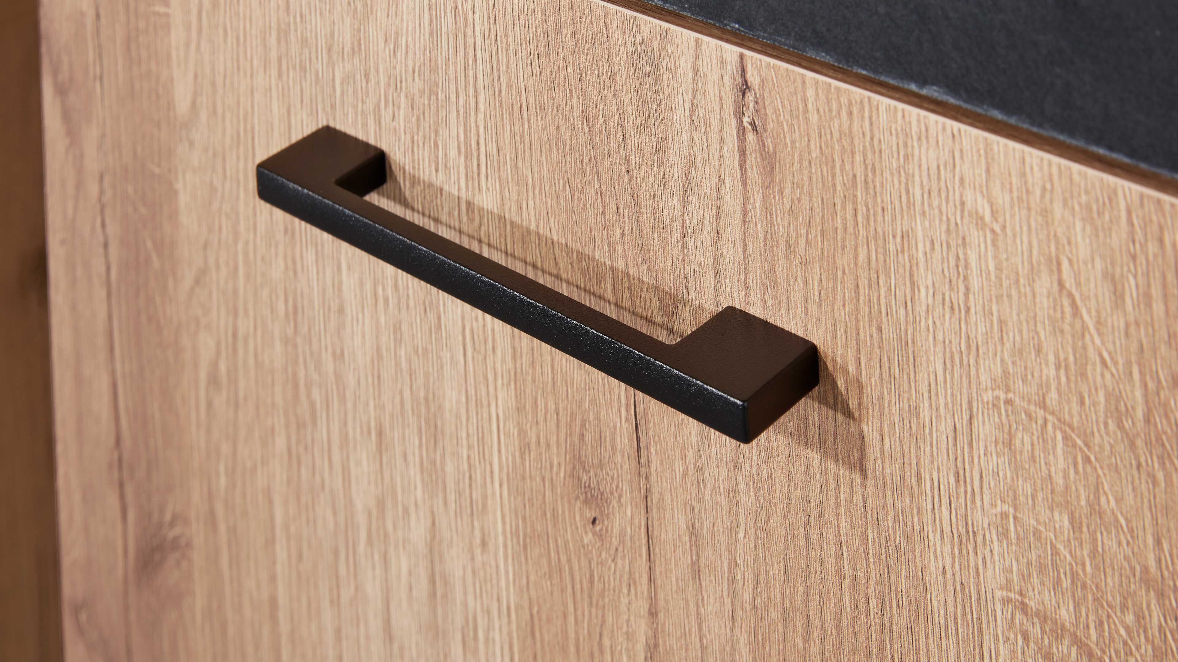 Schwarzer rechteckiger Metallgriff an hellholzfarbener Schranktür mit sichtbarer Holzmaserung und dunkler Arbeitsplattenkante.