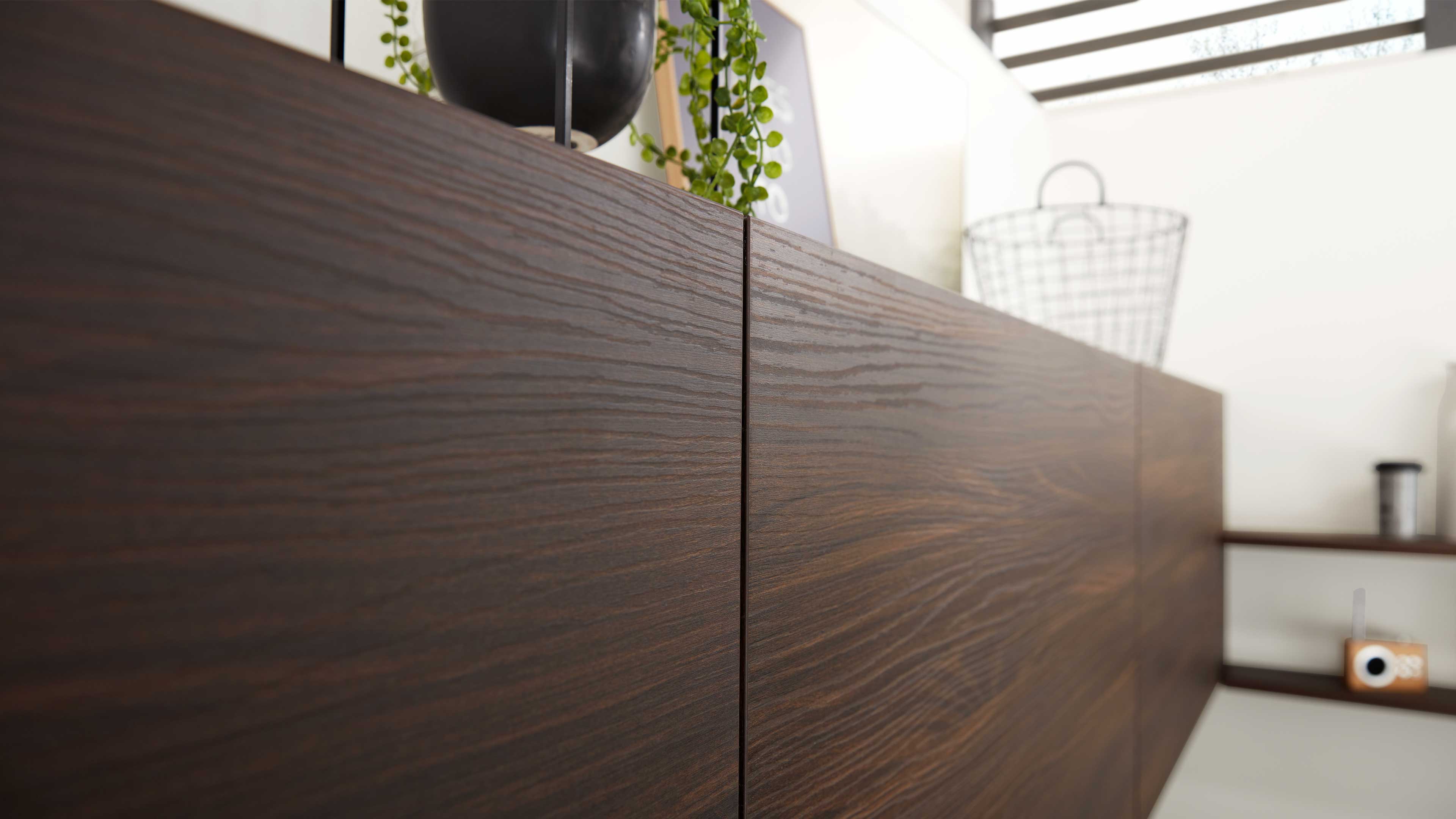 Dunkelbraune Holzfront eines Sideboards mit deutlicher Mittelspalte und sichtbarer Holzmaserung, oben Deko und hängende Pflanze.