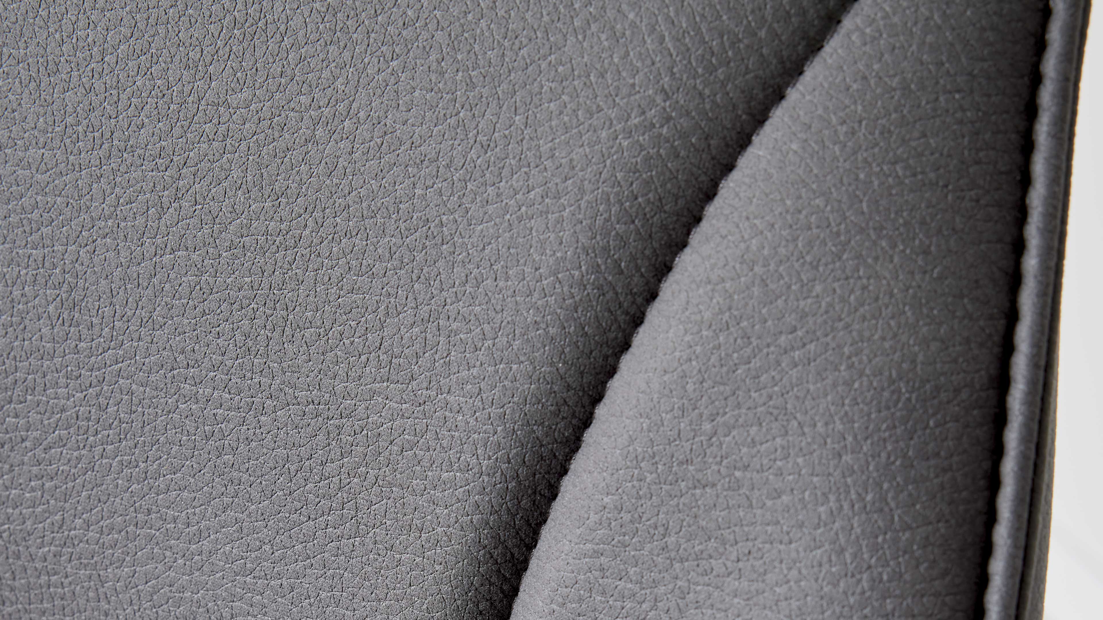 Grau strukturiertes Leder-Polster mit feiner Narbung, einer seitlichen Naht und sichtbarer Polsterung.