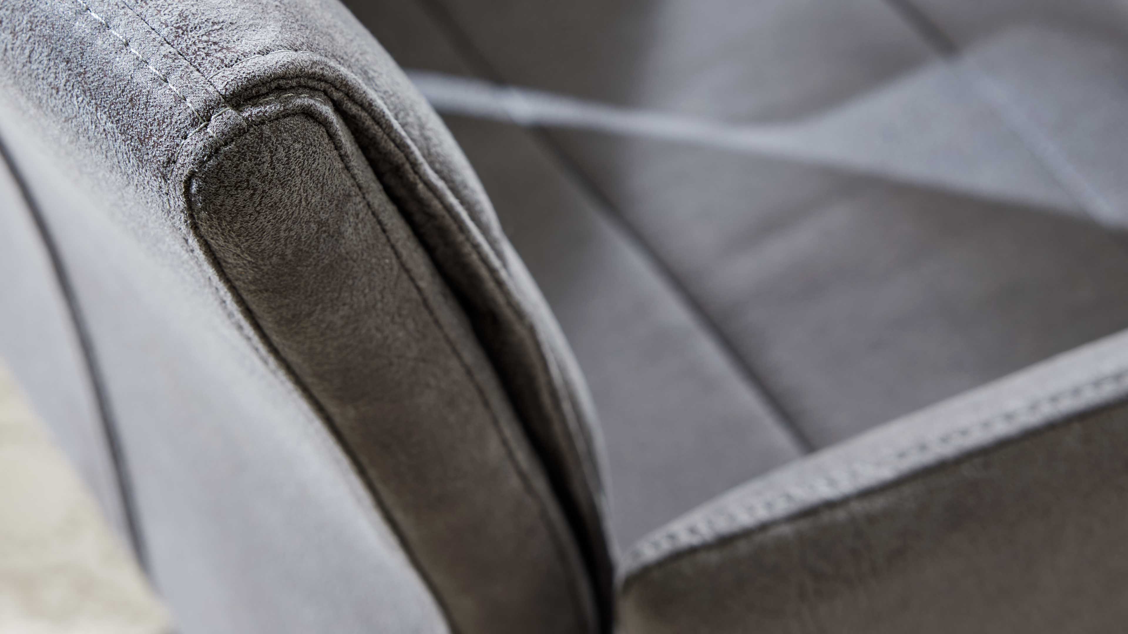 Grau bezogene Armlehne in Nahaufnahme mit sichtbaren Ziernähten und weicher Oberfläche, daneben die gepolsterte Sitzfläche.