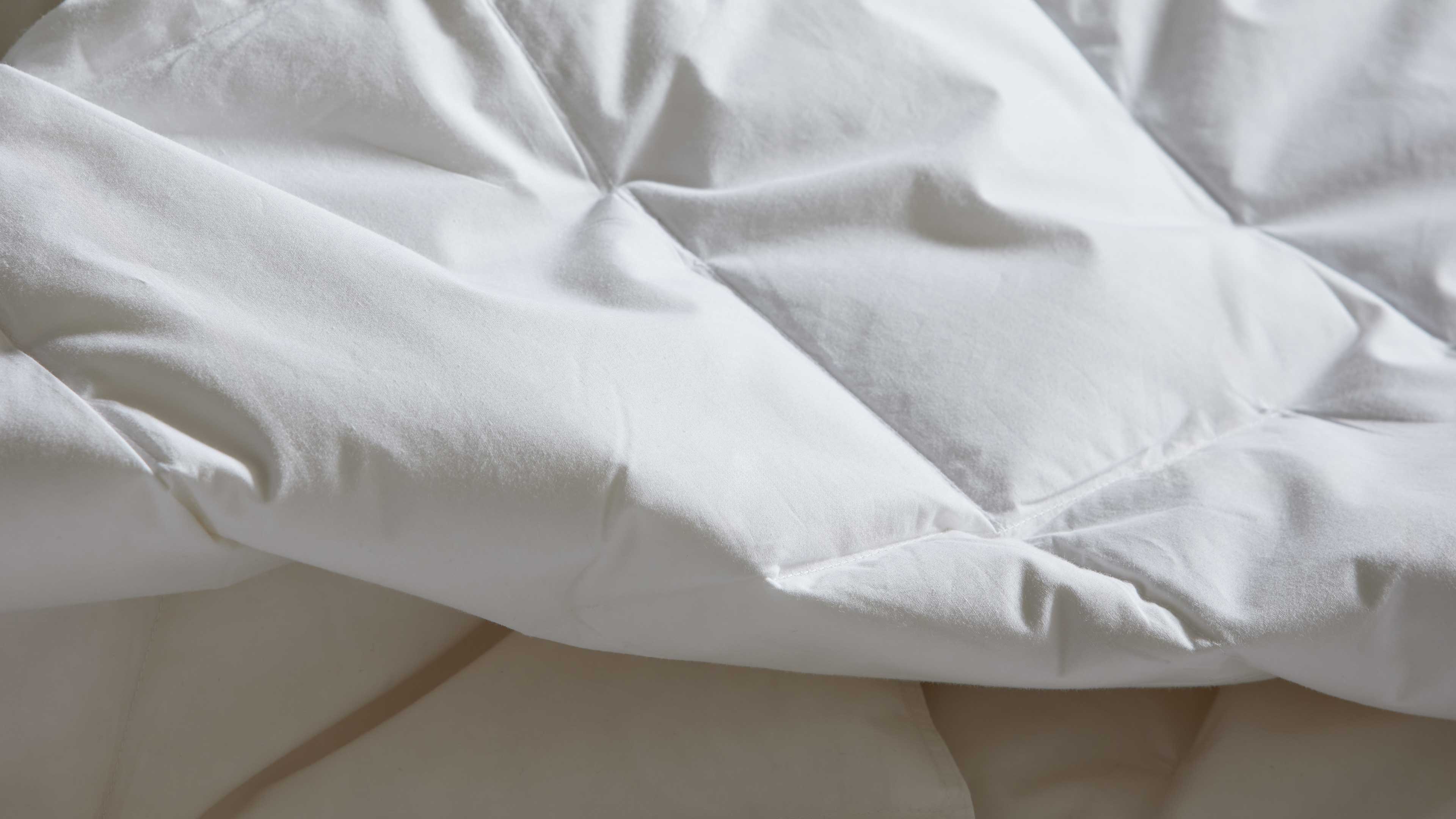 Weiße gesteppte Bettdecke mit quadratischen Kammern, sichtbaren Nähten und weichen Falten in Nahaufnahme.