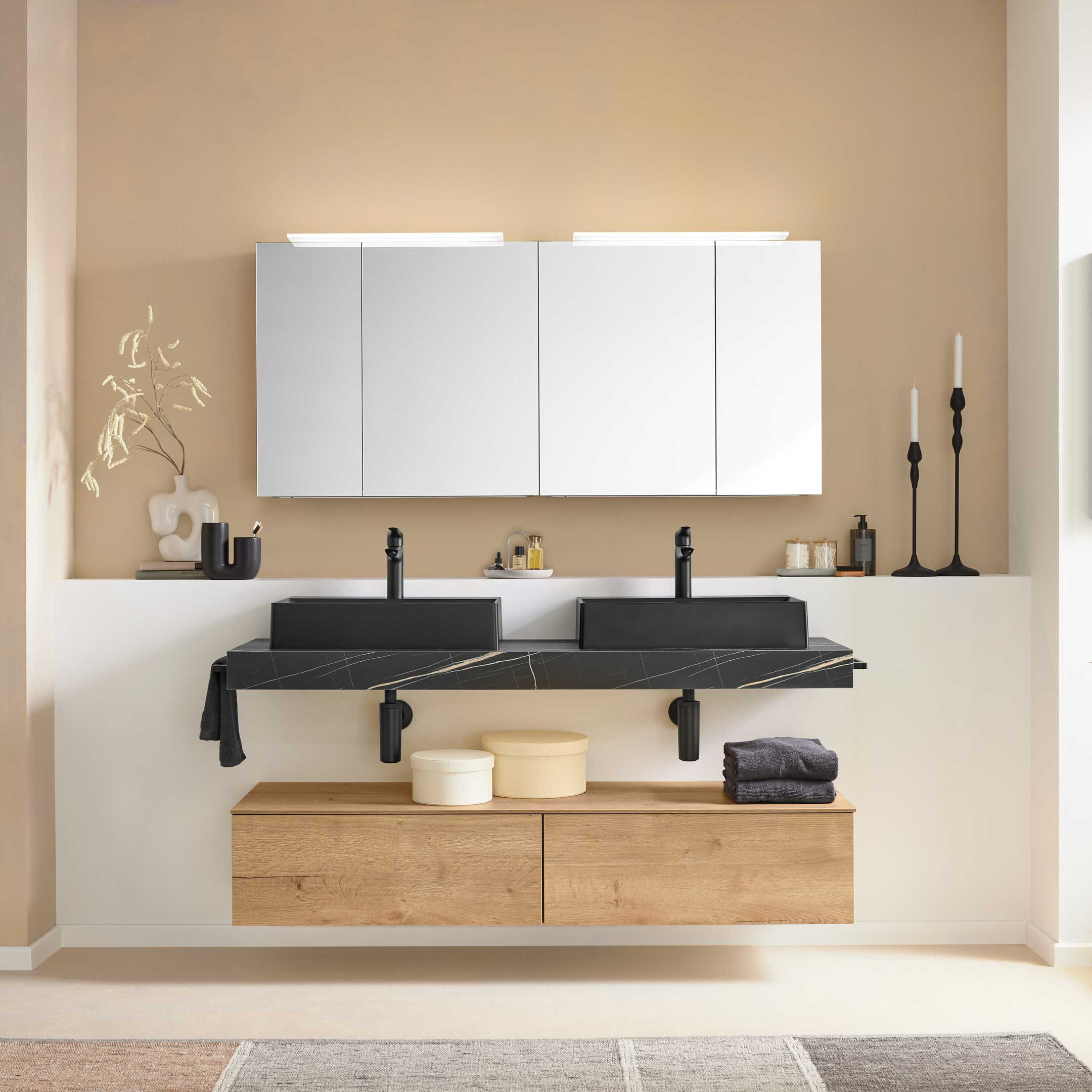 Zweifach-Waschtisch mit schwarzen rechteckigen Becken auf schwarzer Marmorplatte, hängendem Holz-Unterschrank und Spiegelschrank.