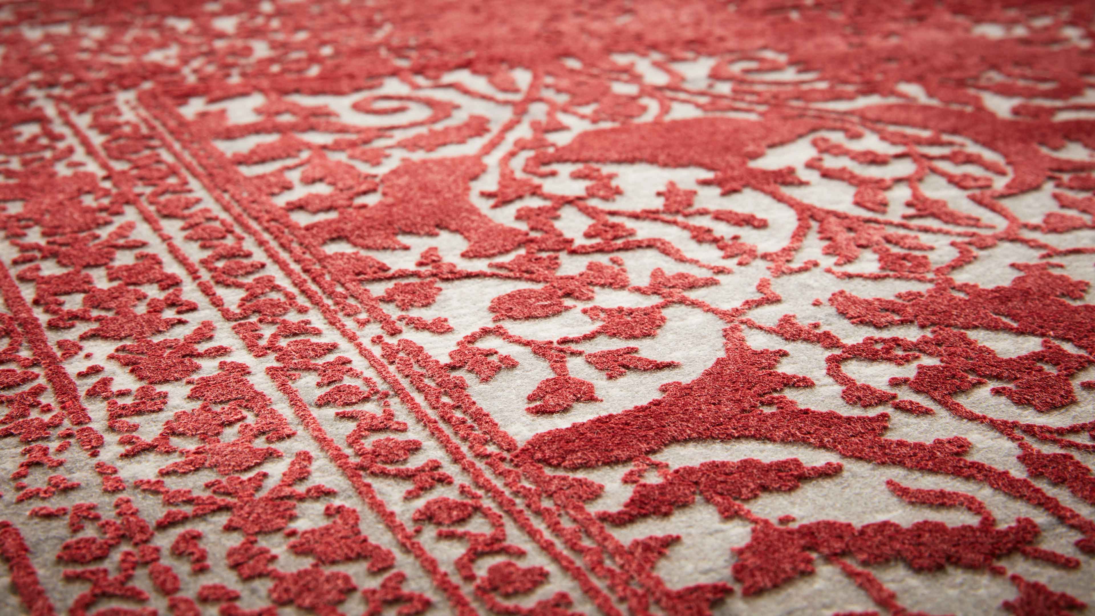 Nahaufnahme eines Teppichs mit erhöhtem roten Ornamentmuster und floralen Bordüren auf beige Grund.