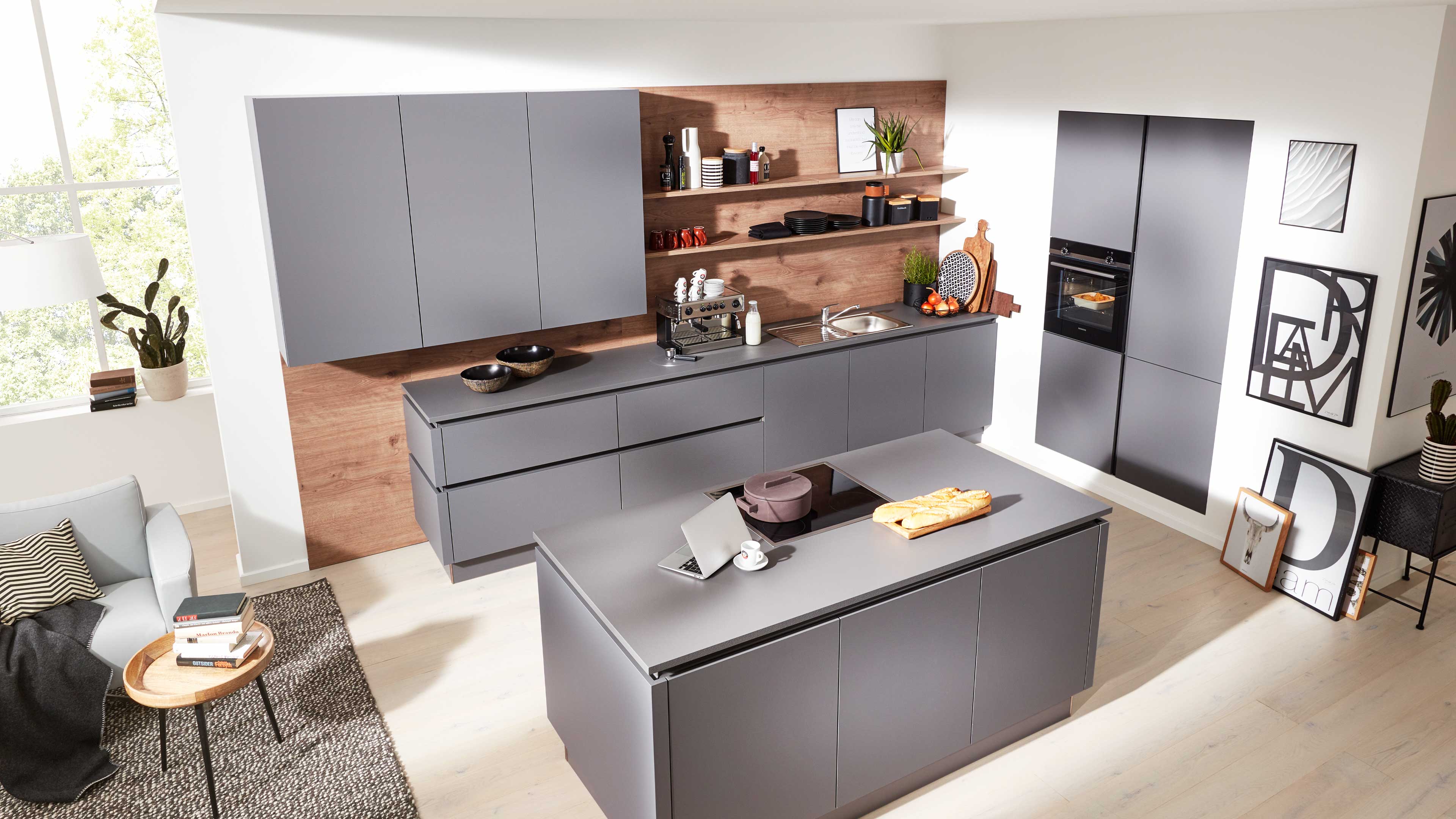 Glatte graue Küchenzeile mit Insel, hölzerner Rückwand und offenen Regalen, eingebautem Ofen, Spüle und Sitzbereich daneben.