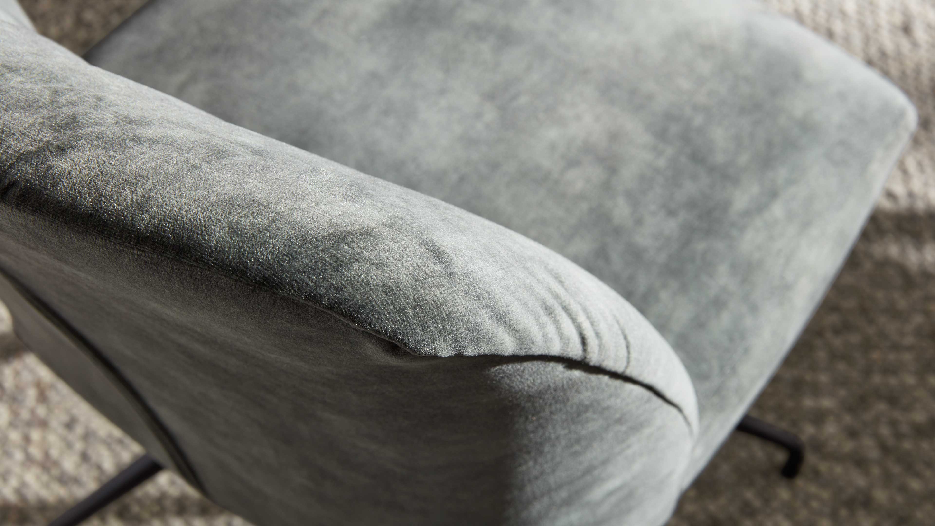 Grau bezogene Polstersessel-Armlehne mit sichtbarer Naht, samtiger Textur und einem schlanken schwarzen Metallfuß.