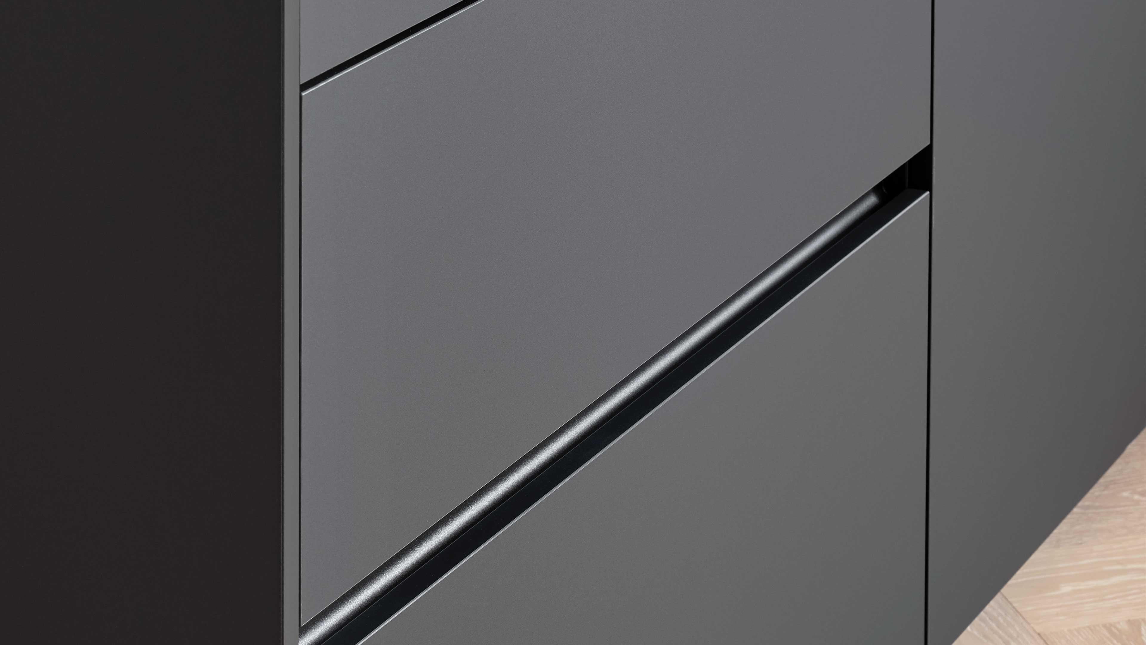 Nahaufnahme einer grauen Schrankfront mit diagonal verlaufender schwarzer Griffmulde, sichtbaren Fugen und hellem Parkettboden.