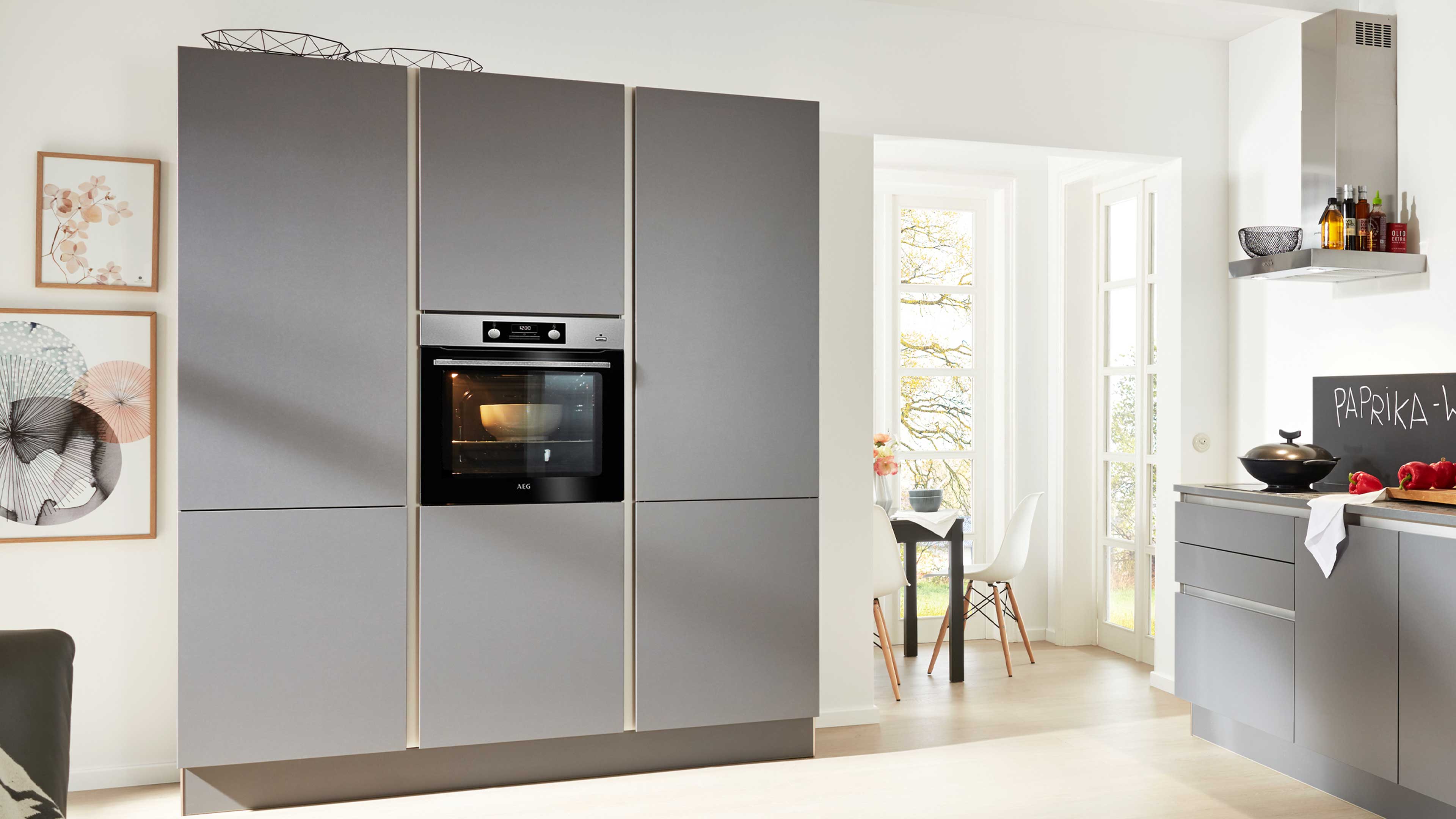 Grifflose Einbauküche mit hohen, matten grauen Schrankfronten, eingelassenem schwarzen Backofen mit Edelstahlrahmen.