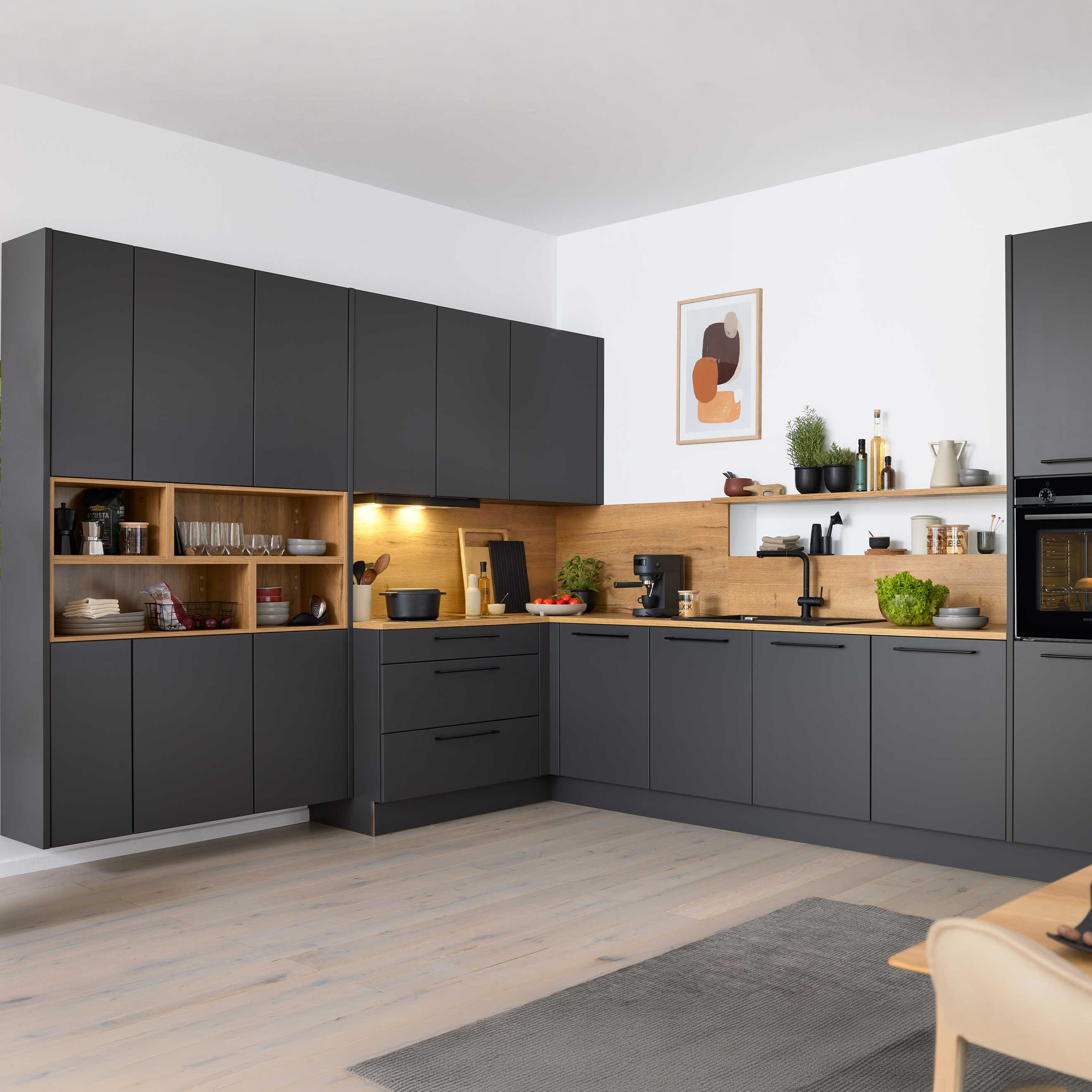 Dunkelgraue L-förmige Küchenzeile mit Holzarbeitsplatte und Holzregalen, eingebautem Ofen, schwarzem Hahn und Kaffeemaschine.