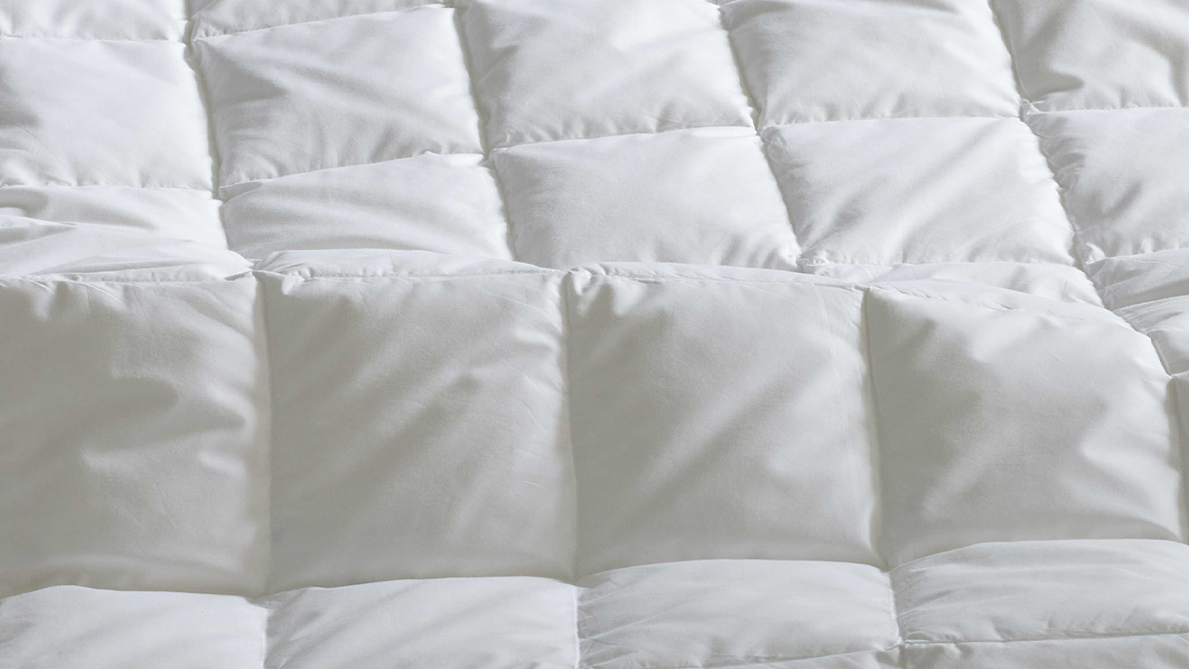 Gesteppte weiße Bettdecke mit großen quadratischen Steppkammern, sichtbaren Nähten und gleichmäßig gepolsterter Oberfläche.