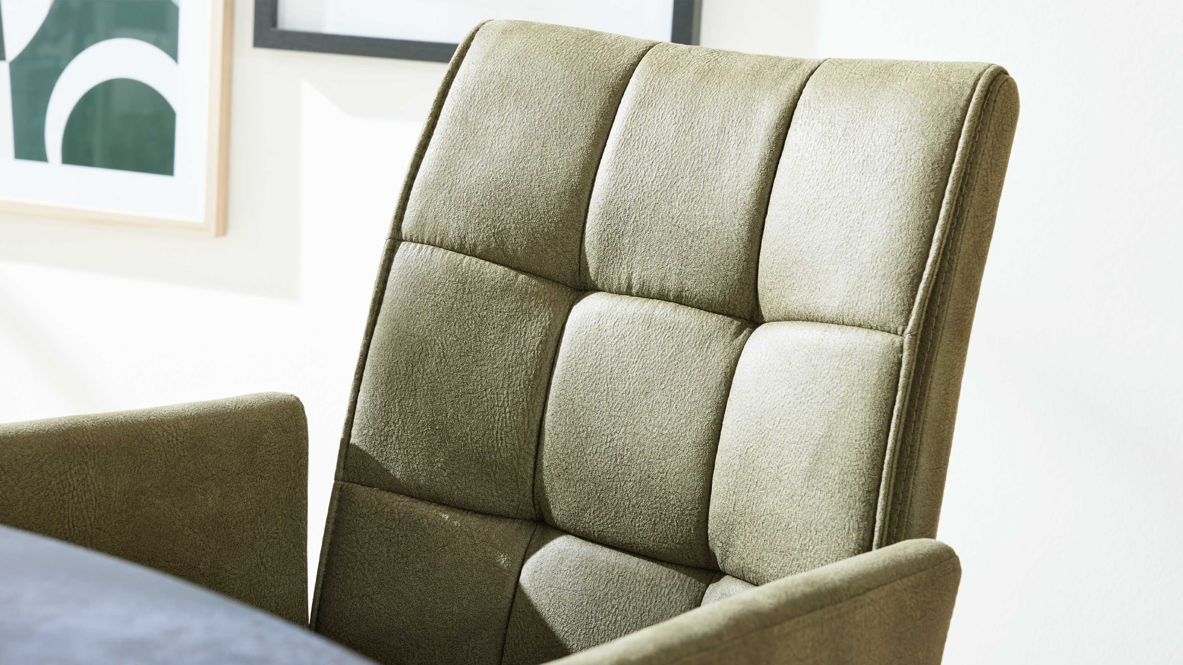 Olivegrüne, gepolsterte Stuhllehne mit quadratischen Steppungen und sichtbarer Armlehne vor einer hellen Wand.