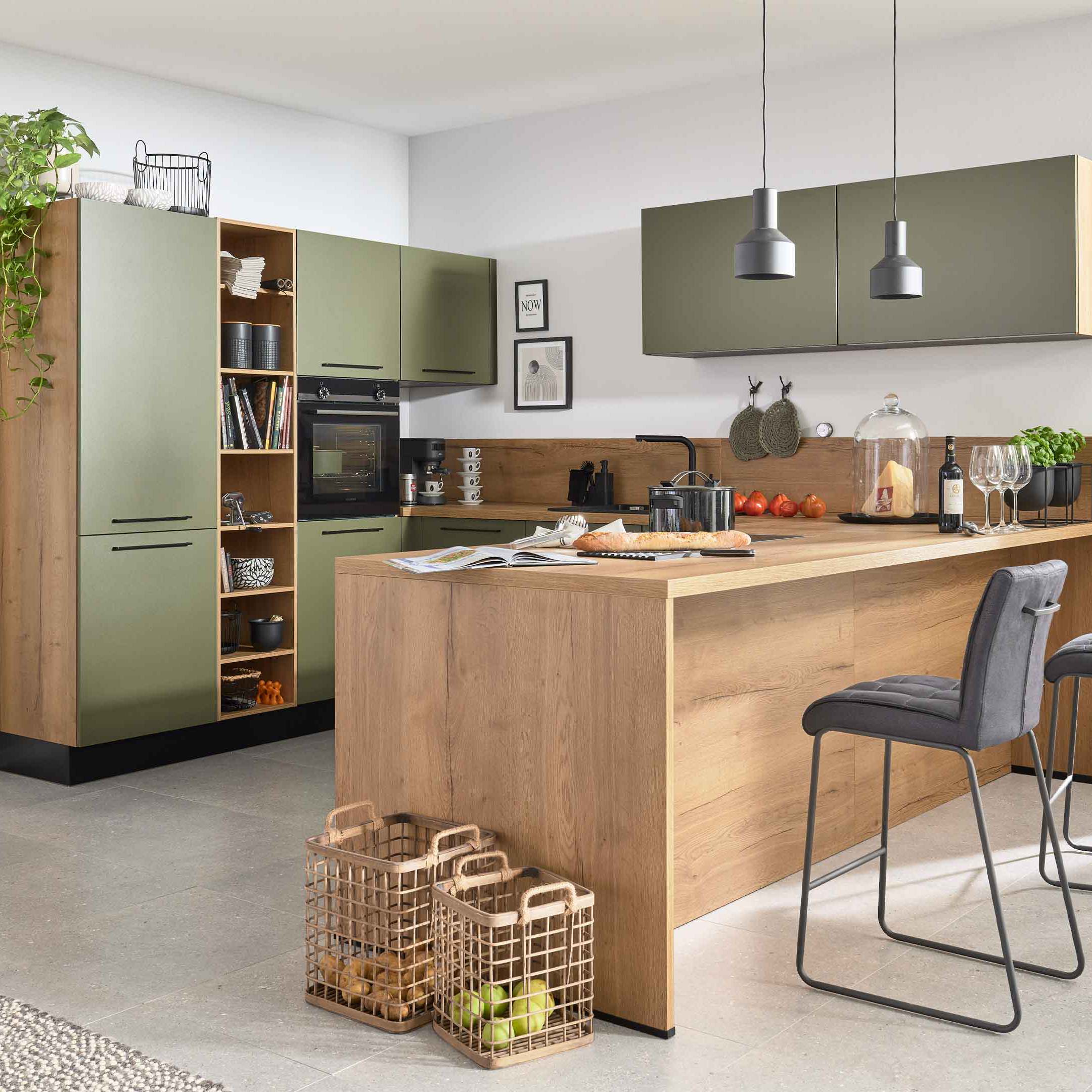 Holz-Kücheninsel mit Arbeitsfläche, zwei grauen Barhockern und Körben am Fuß; grüne Hochschränke mit offenem Regal.