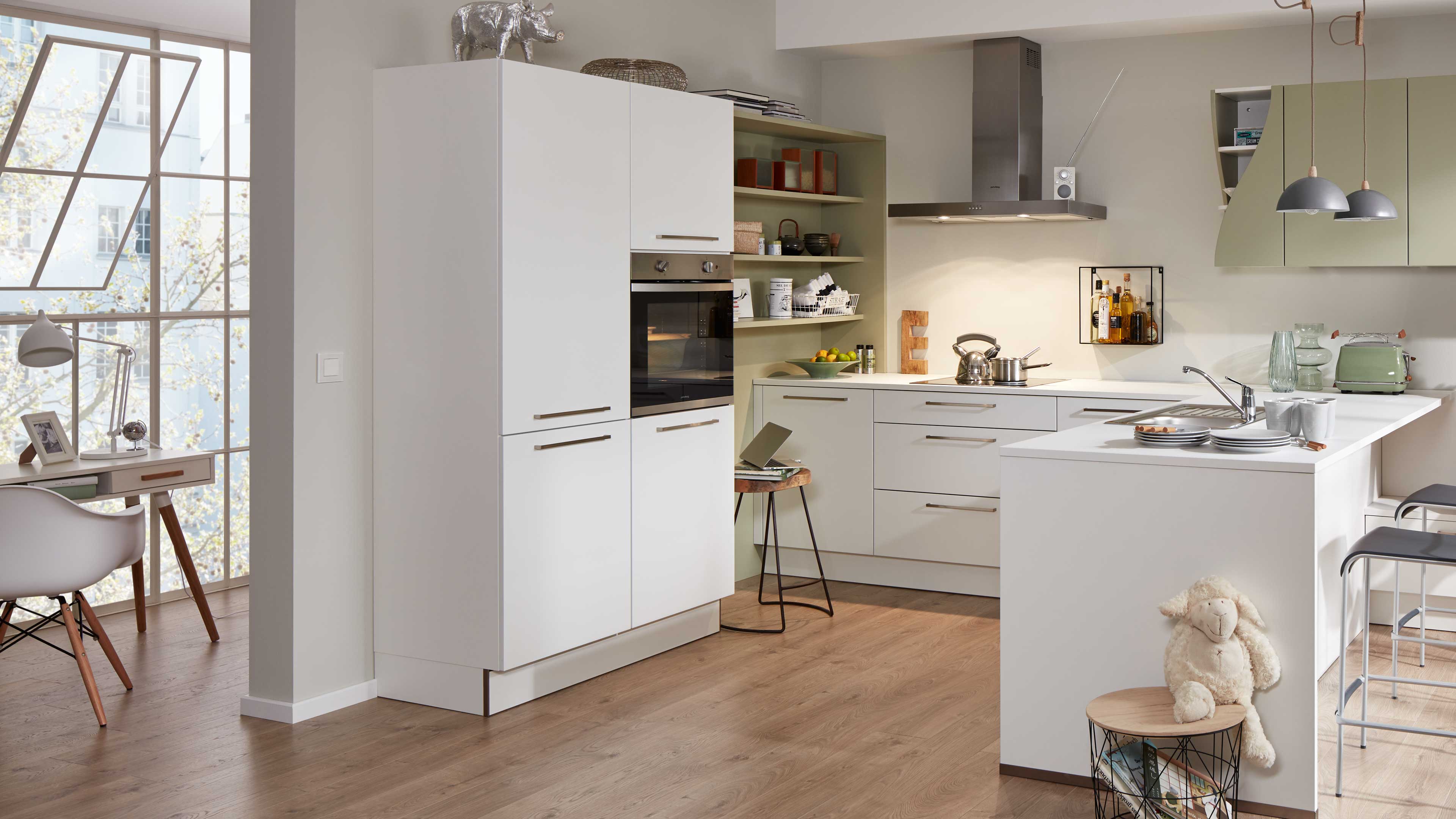 weißes, mattes Küchenprogramm mit hohem Schrank und integriertem Backofen, offenen grünen Regalen, Insel mit Spüle und Edelstahl-Dunstabzug.