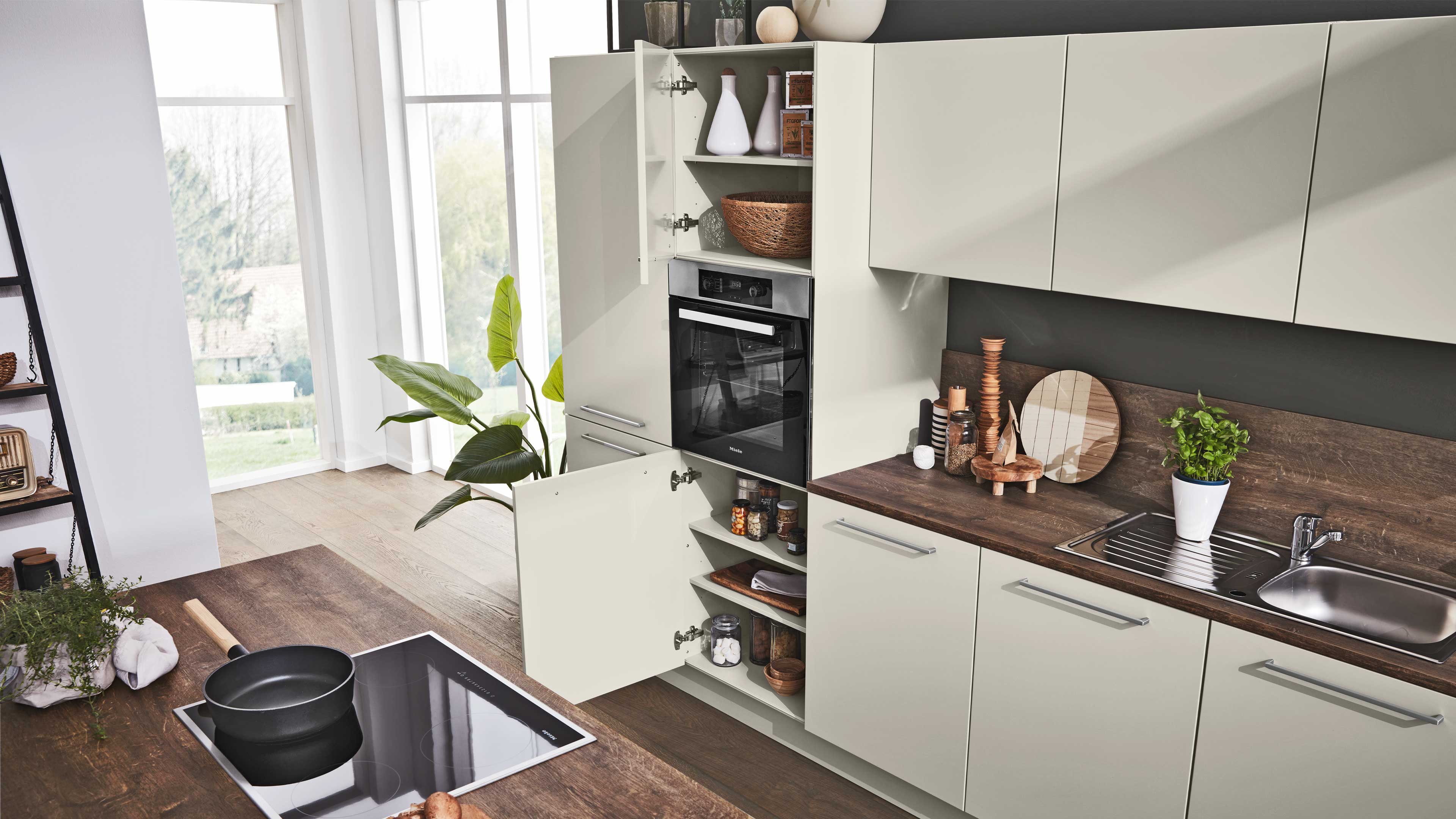 Helle Küchenzeile mit offenem Hochschrank und eingebautem Backofen, Regalböden mit Schalen, Gläsern und Holzarbeitsplatte.