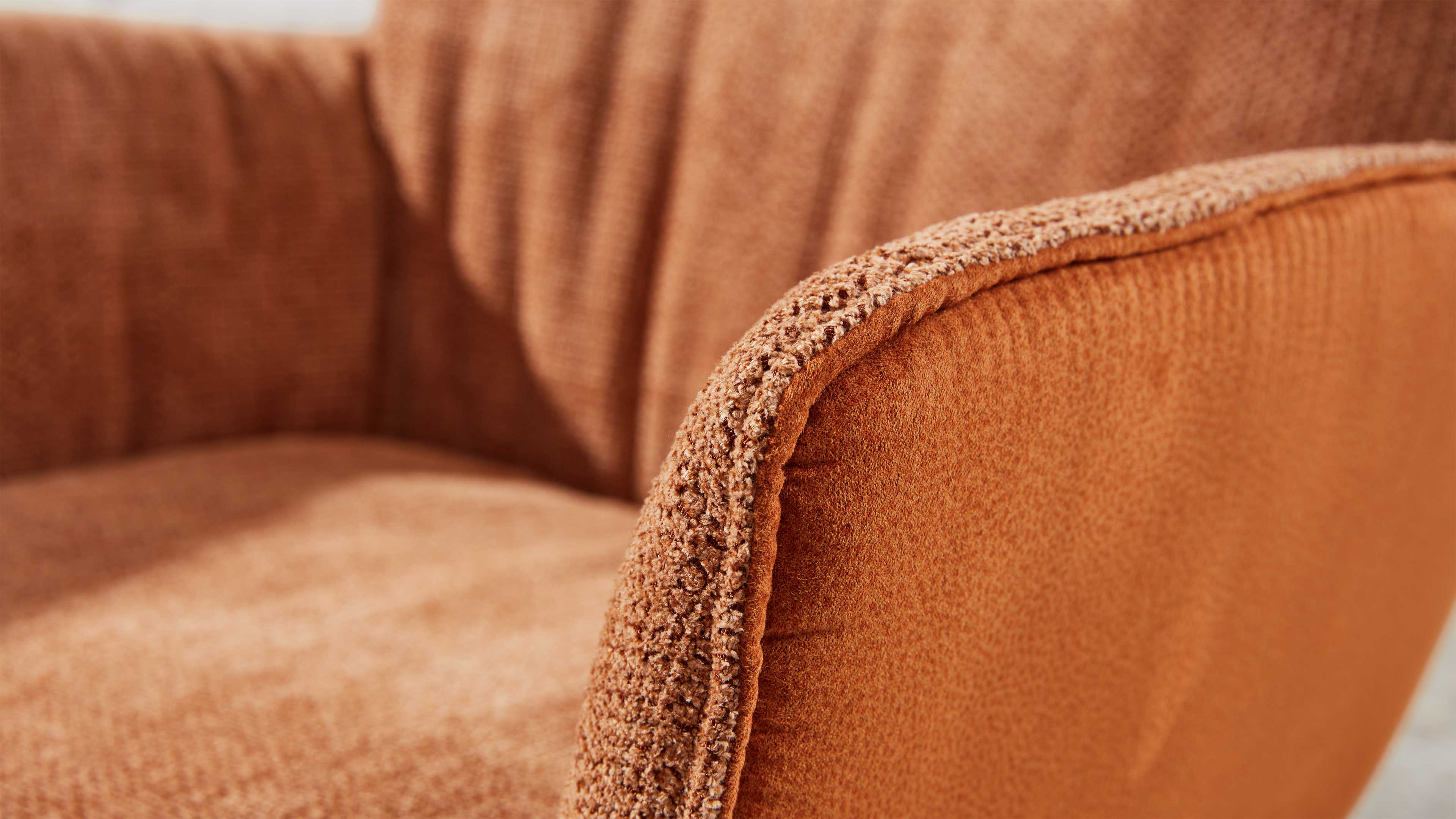 Armlehne eines orangefarbenen Sessels mit grob strukturierter Bouclé-Kante, sichtbare Sitzfläche und gerundete Rückenlehne.